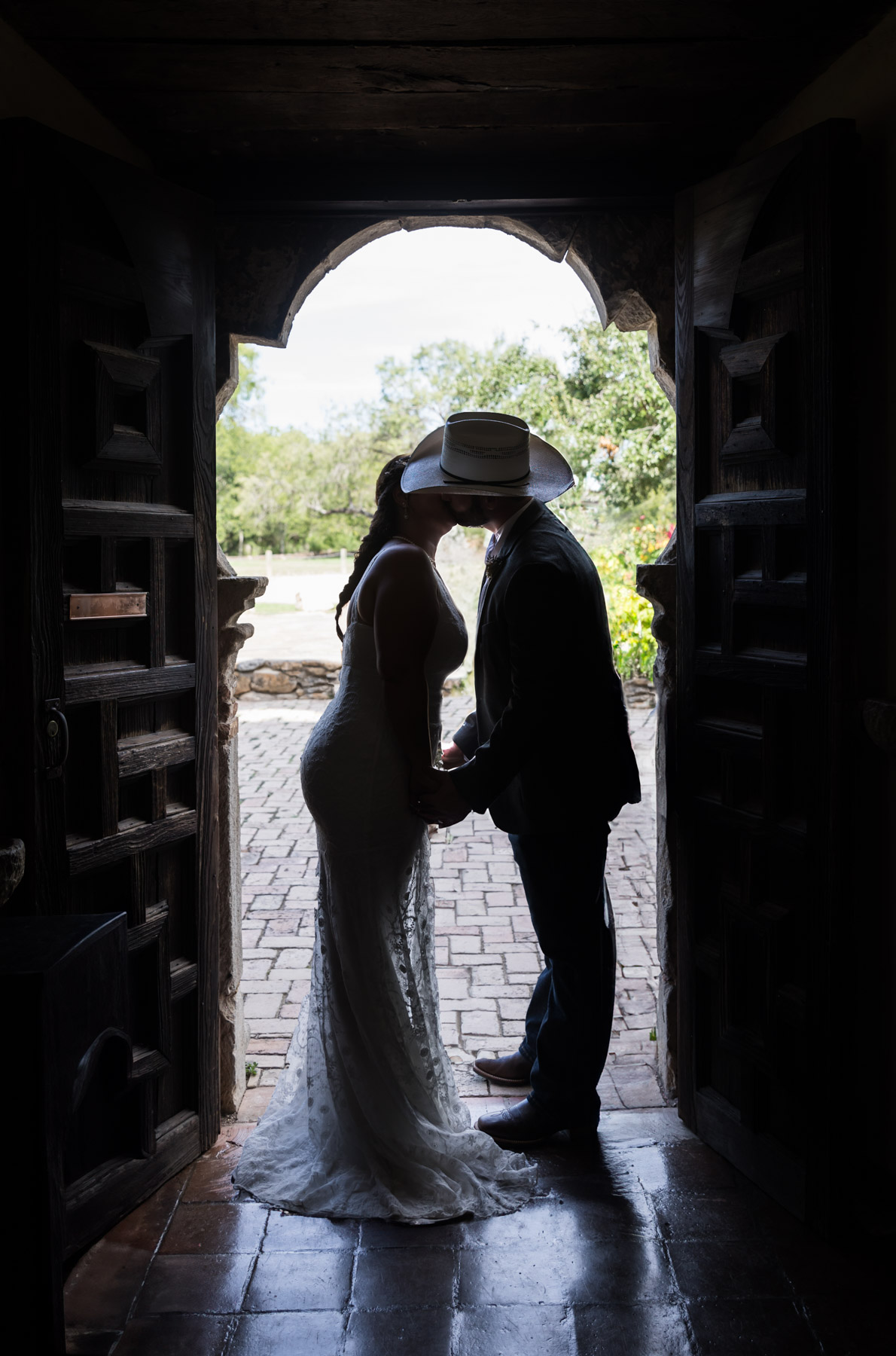 Silhouette of bride and groom kissing in ornate doorway for an article on how to get married at Mission Espada