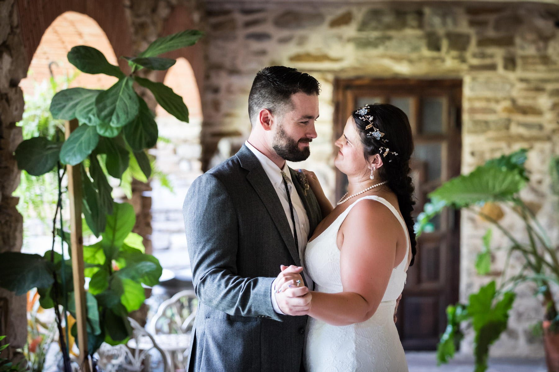 Bride in white sleeveless dress and groom wearing grey jacket dancing under covered walkway for an article on how to get married at Mission Espada