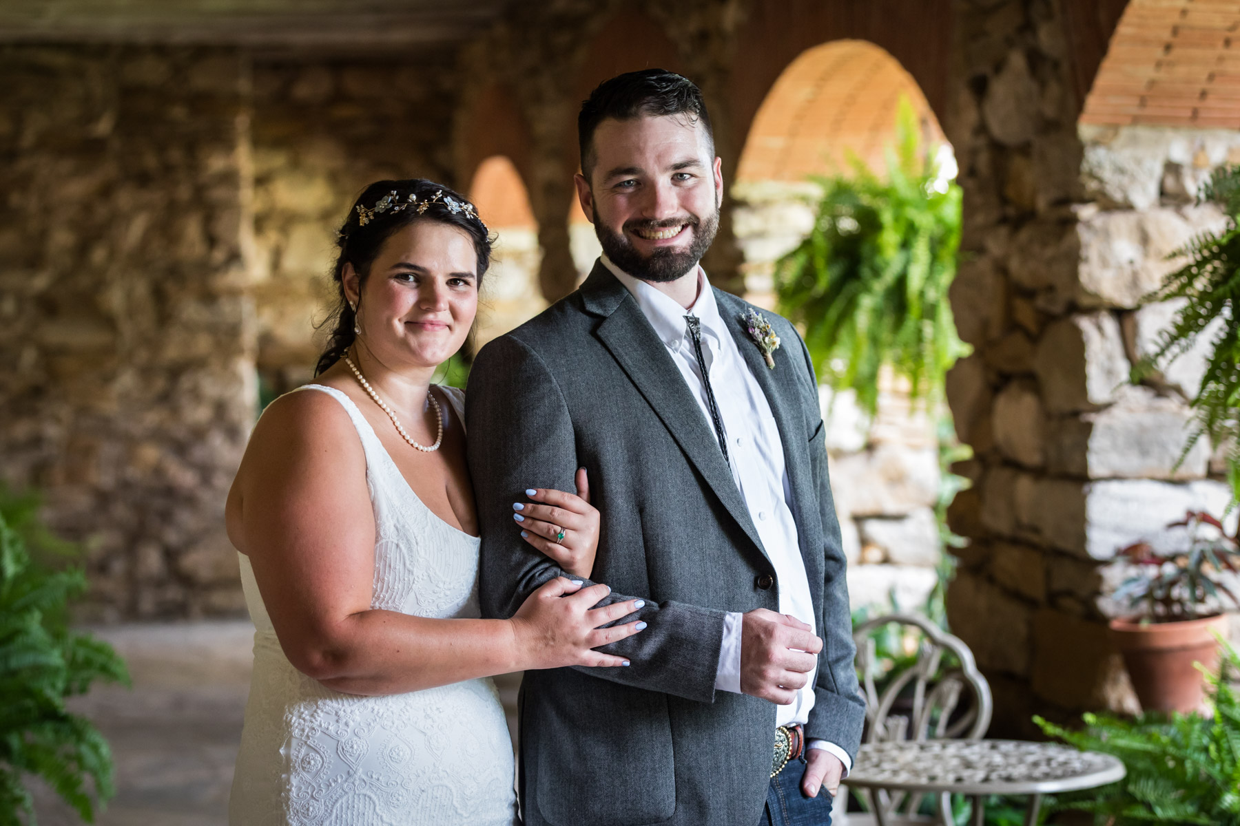 Bride in white sleeveless dress and groom wearing grey jacket under covered walkway for an article on how to get married at Mission Espada