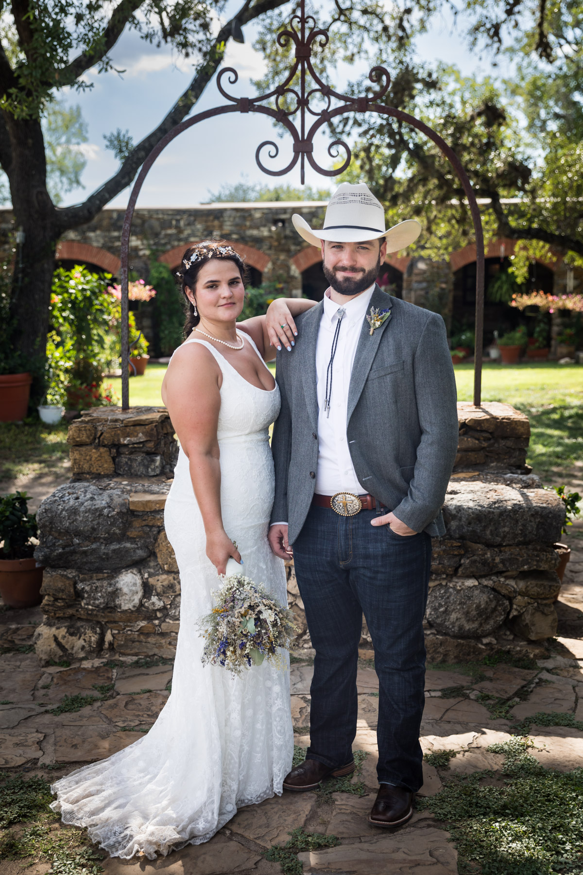 Bride and groom standing in front of stone well for an article on how to get married at Mission Espada