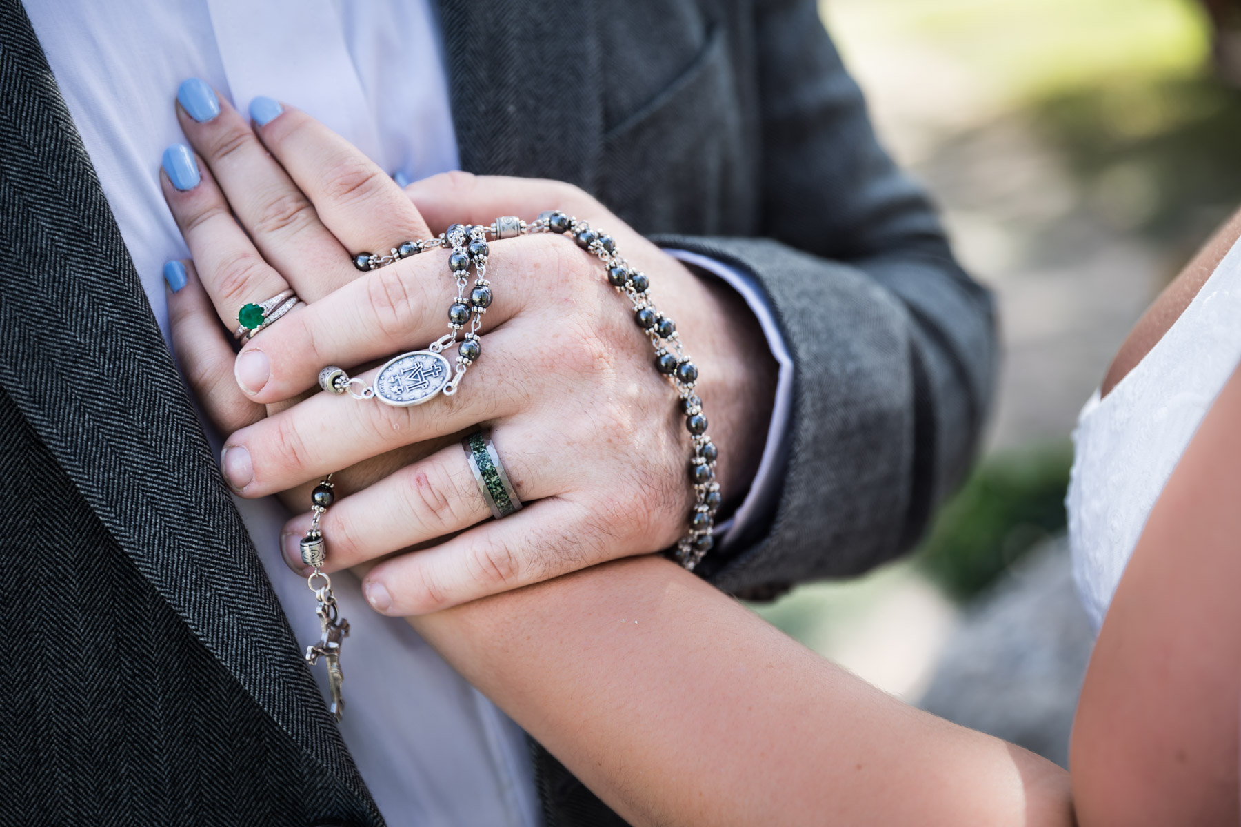 Close up of bride and groom holding hands with rosary draped over hands