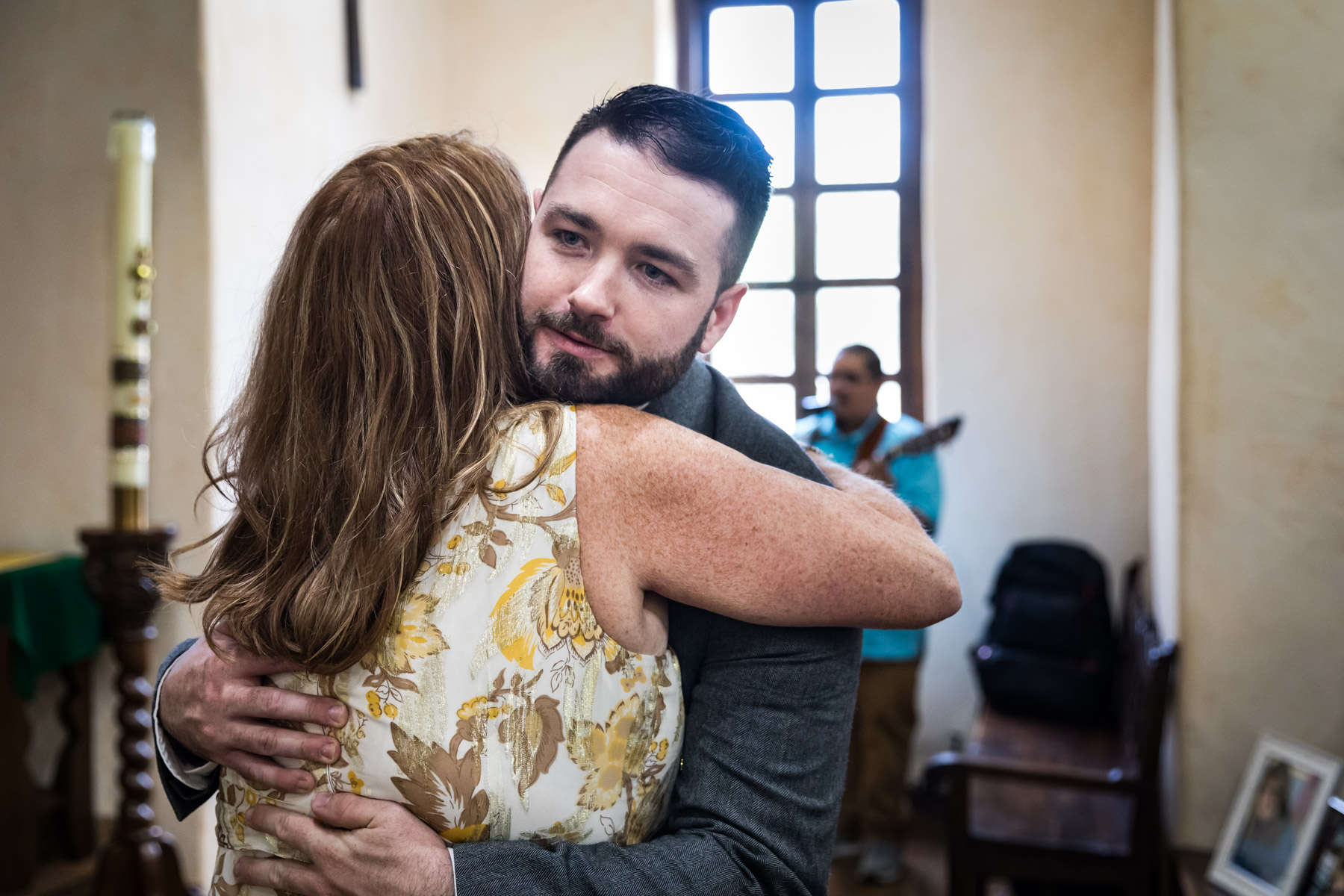 Groom hugging mother in front of window for an article on how to get married at Mission Espada