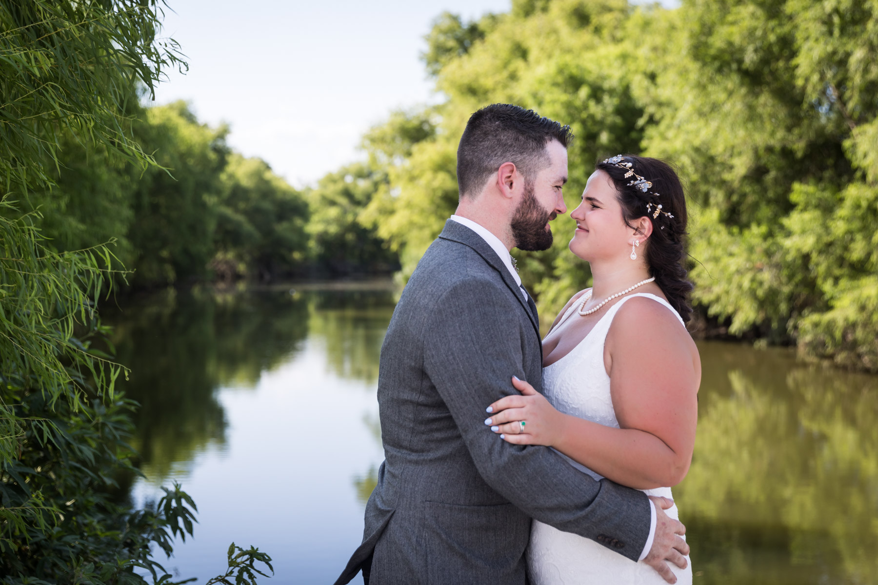 Bride and groom hugging in front of San Antonio River and green trees