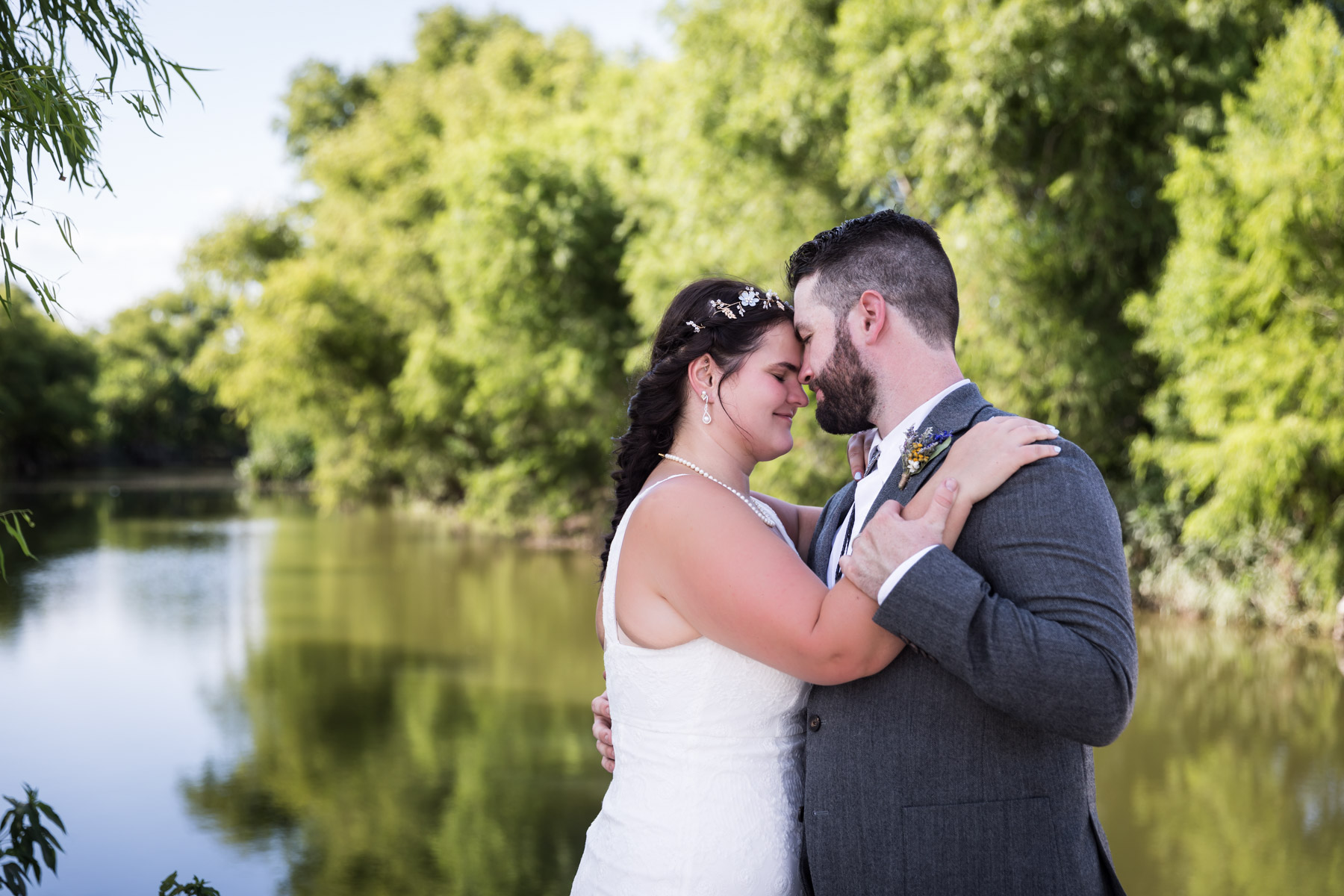 Bride and groom hugging in front of San Antonio River and green trees