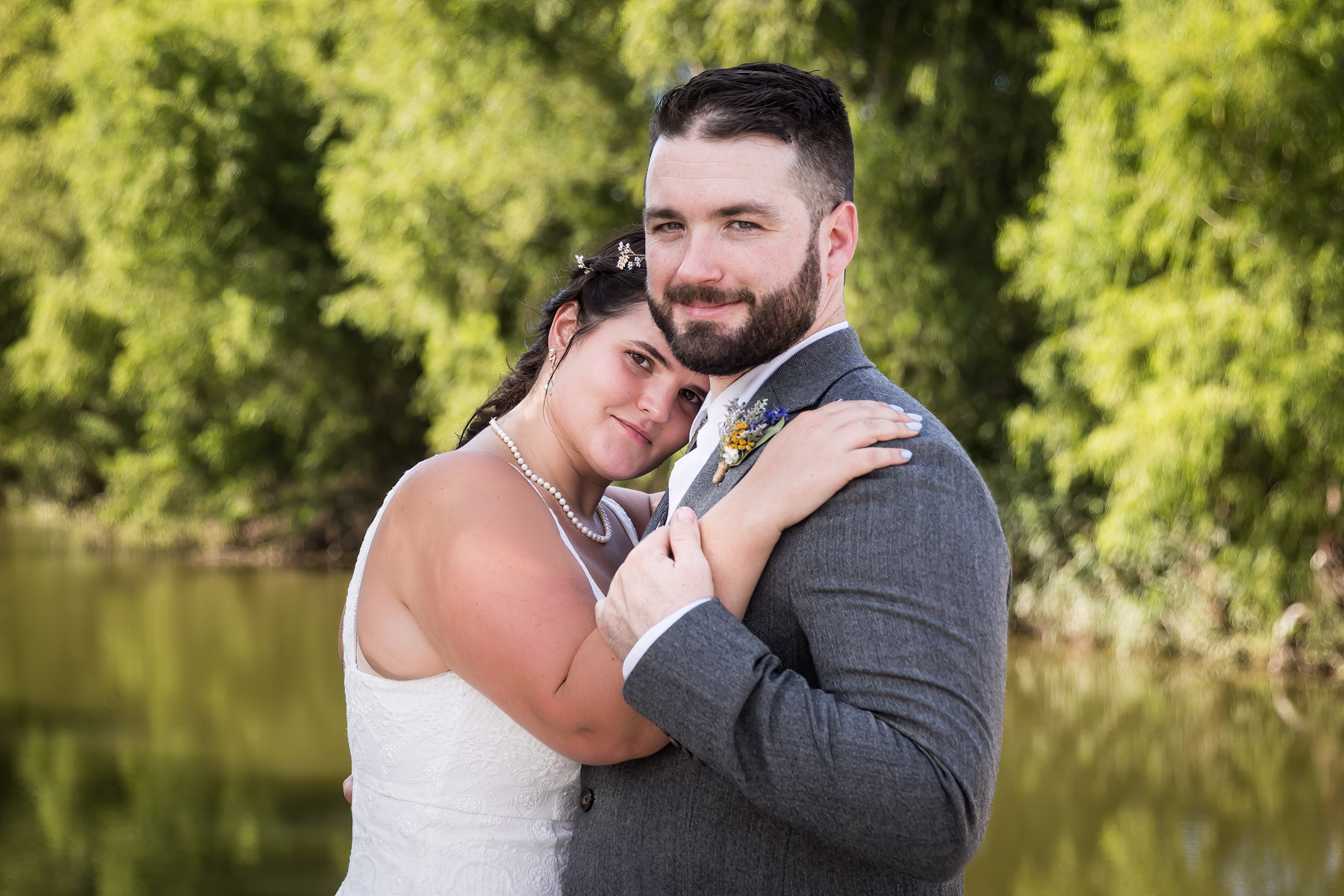 Bride and groom hugging in front of San Antonio River and green trees