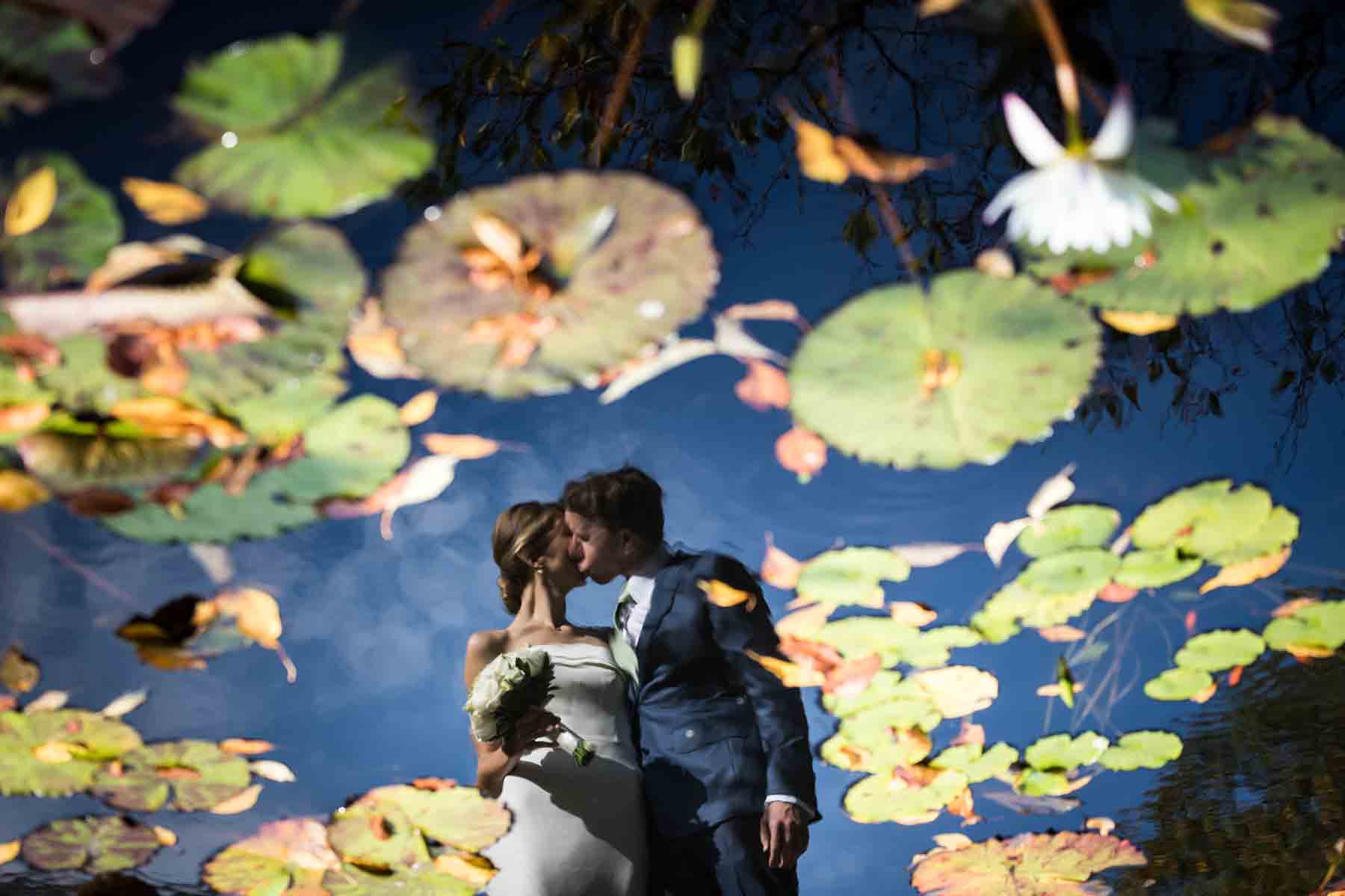 Reflection in lake full of lily ponds of bride and groom kissing for an article on how to have an eco-friendly wedding