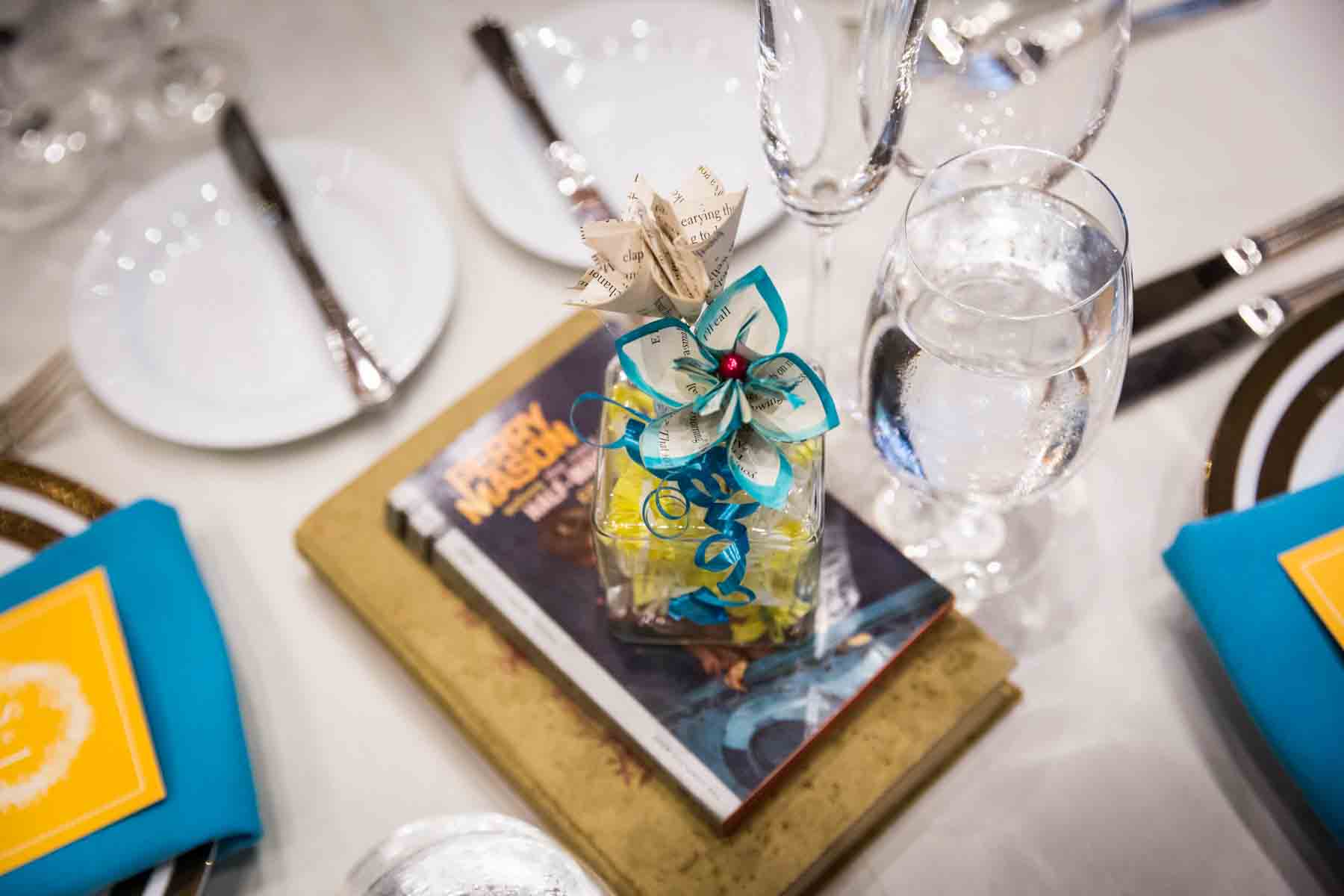 Table centerpiece made of books and glass vase with paper flowers and blue ribbon