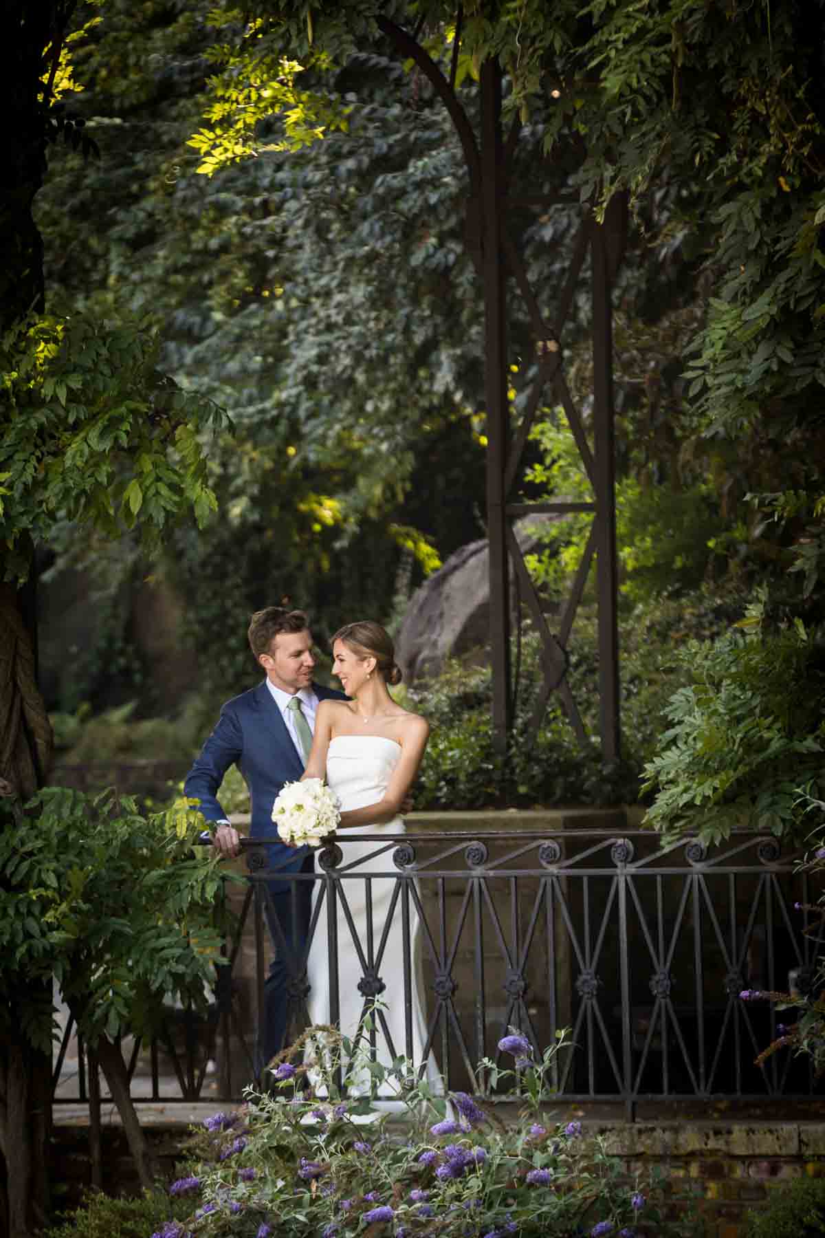 Bride and groom looking at each other behind railing and in front of trees for an article on how to have an eco-friendly wedding