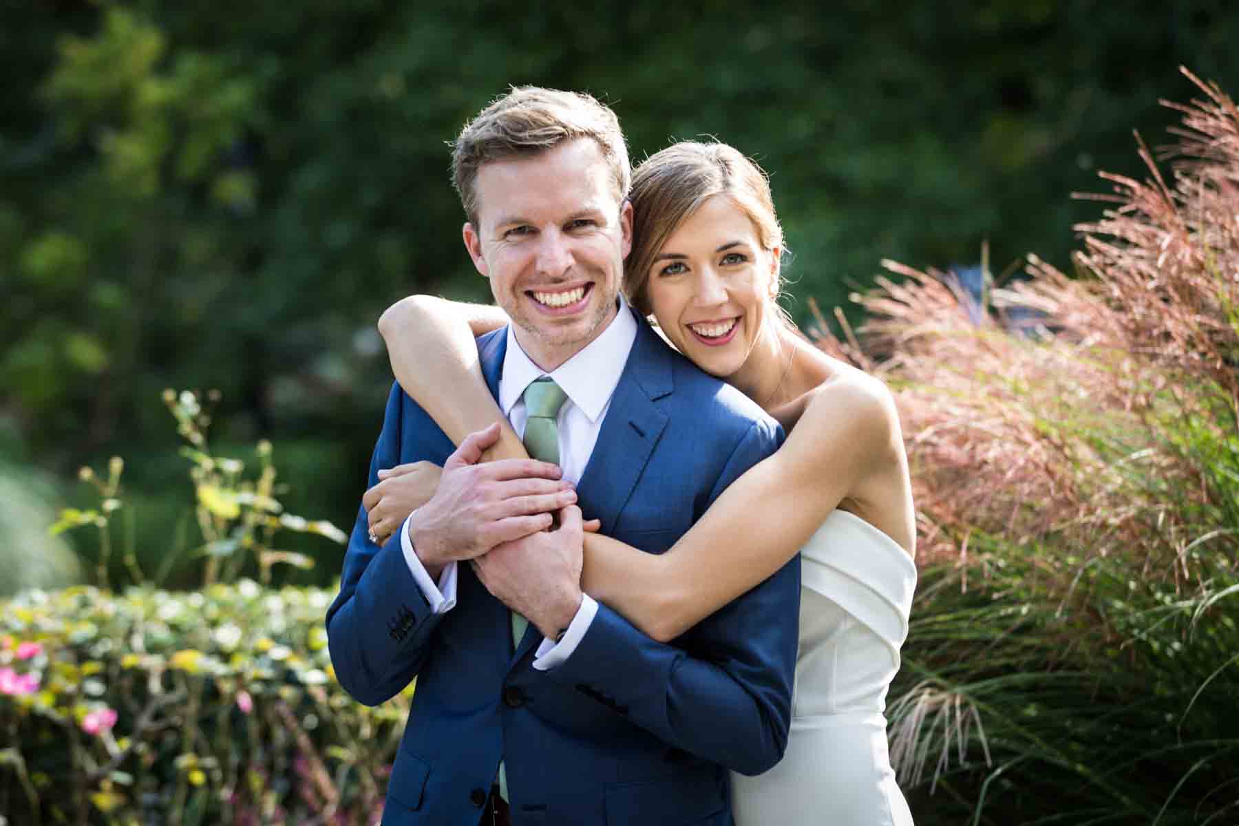 Bride and groom hugging in front of reeds and green plants for an article on how to have an eco-friendly wedding