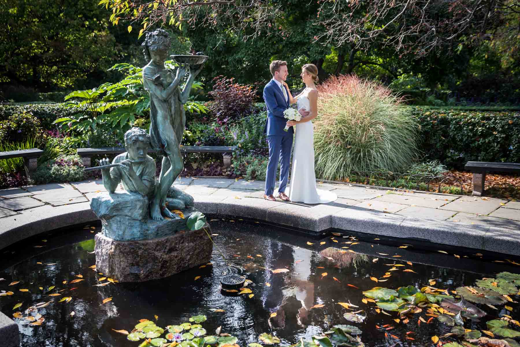 Bride and groom looking at each other on side of pond with bronze statue to the left