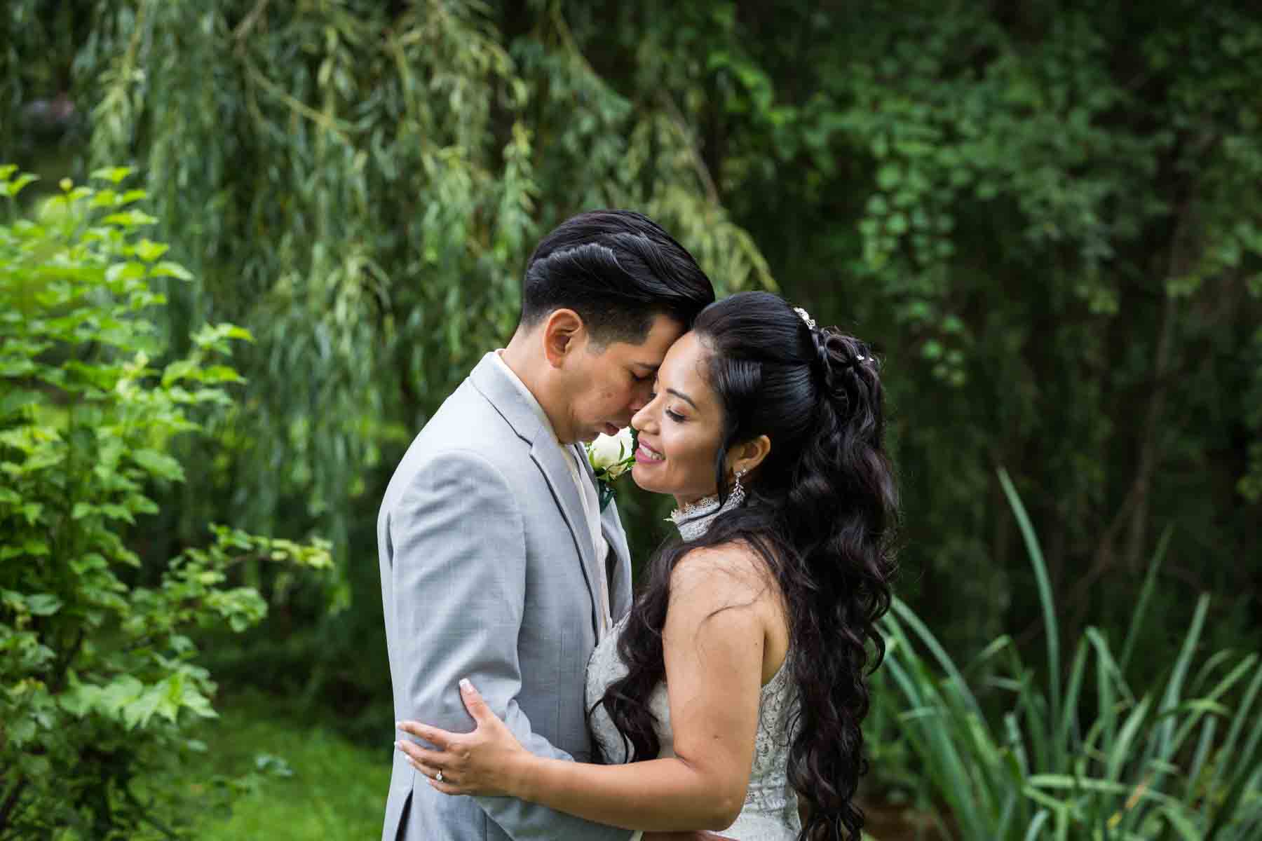 Bride and groom hugging in front of trees and plants for an article on how to have an eco-friendly wedding