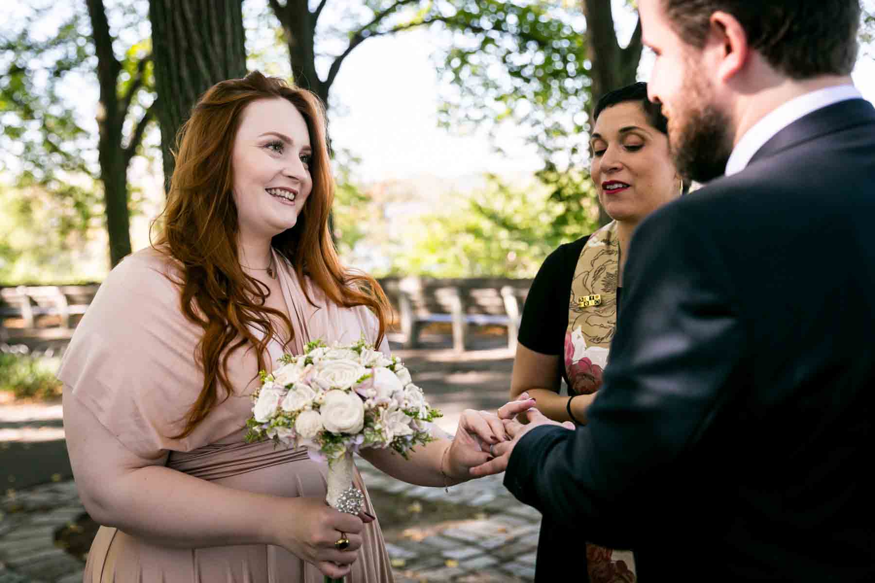 Bride holding flowers and putting ring on groom's finger in park for an article on how to have an eco-friendly wedding