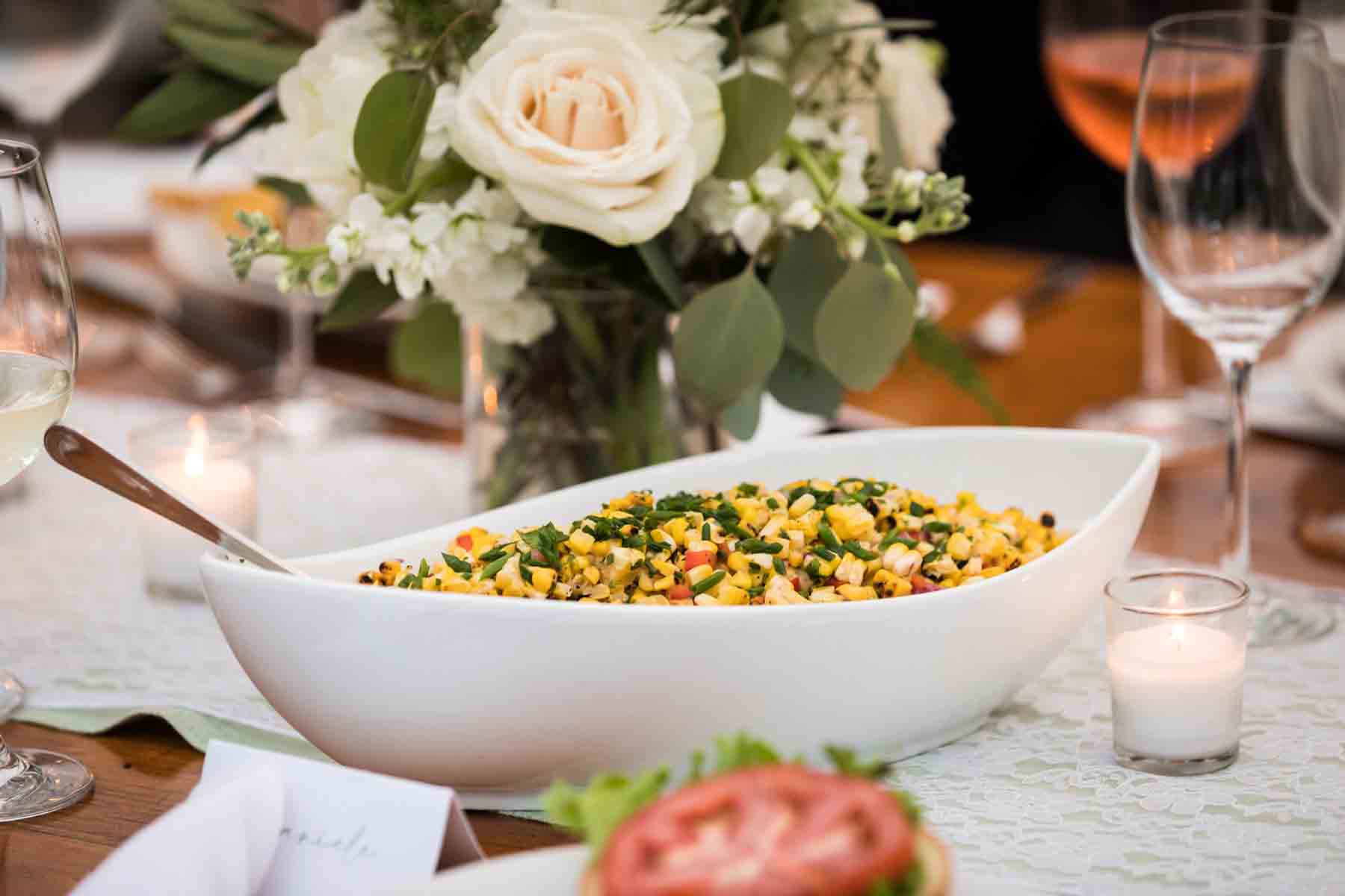 Close up on white bowl filled with yellow corn in front of flower bouquet