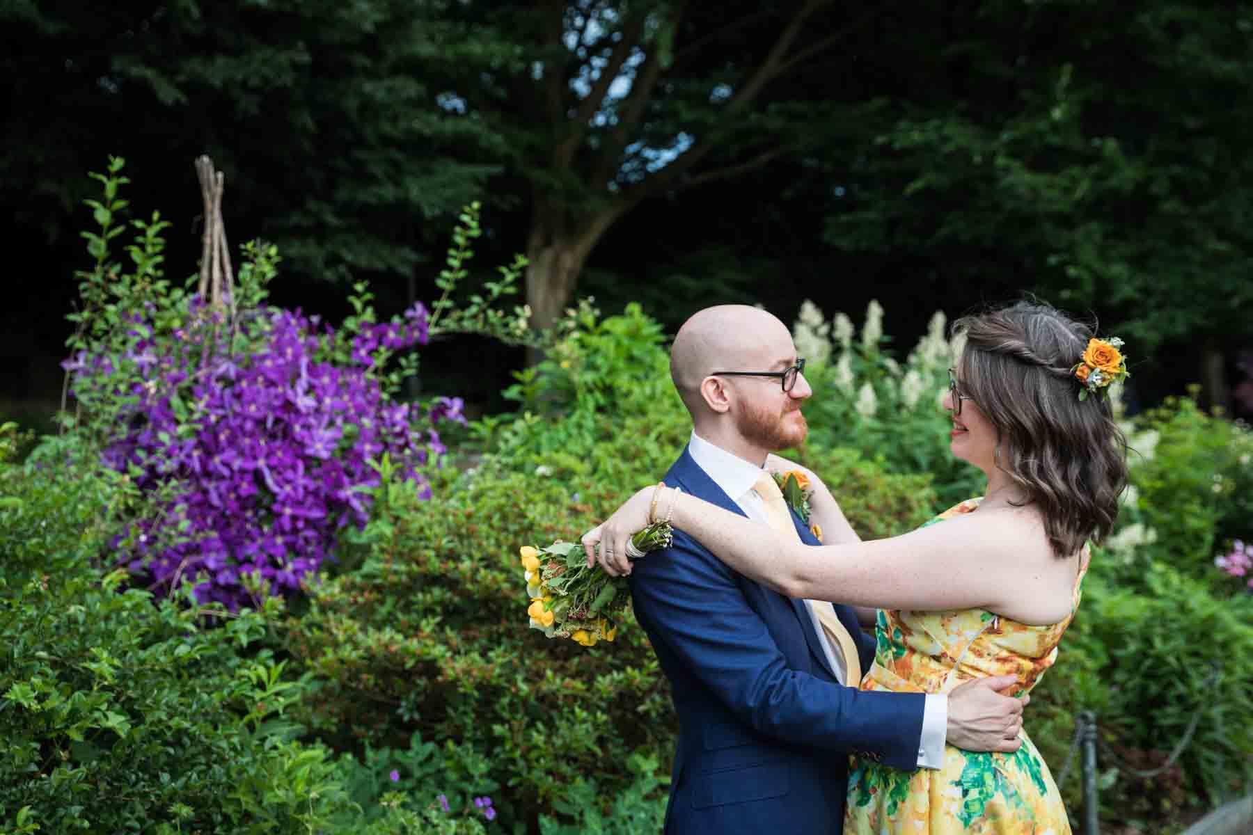 Bride and groom hugging in front of plants and purple flowers for an article on how to have an eco-friendly wedding