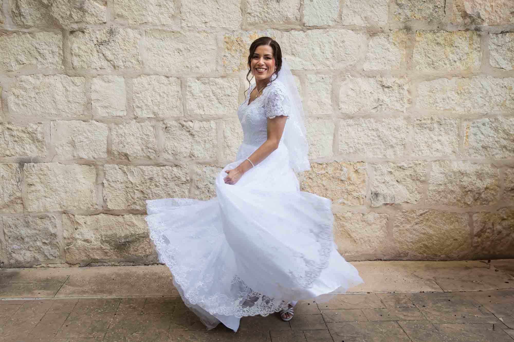 Bride posing in white dress with veil in front of beige, brick wall for an article about a downtown San Antonio bridal portrait session