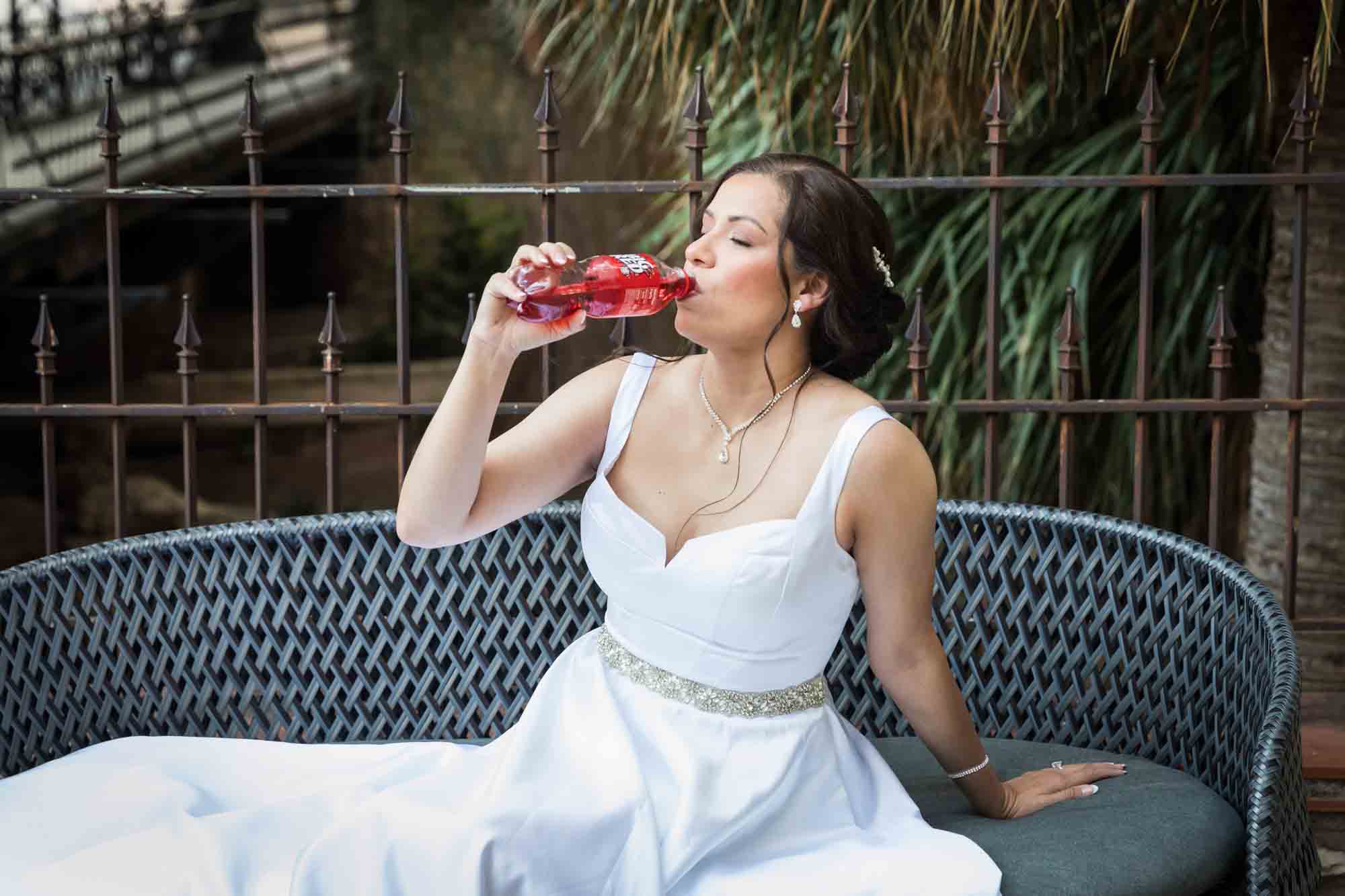 Bride in white dress drinking from a Big Red soda bottle during a downtown San Antonio bridal portrait session