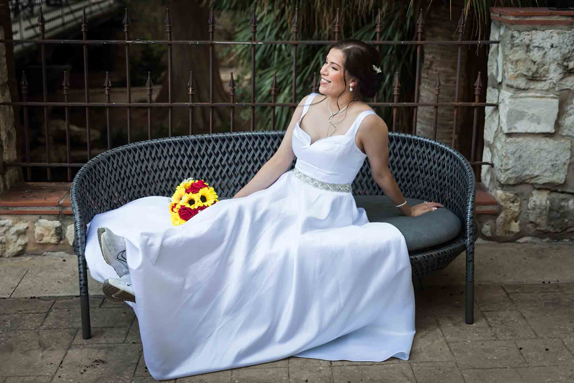 Bride in white dress seated on couch with flower bouquet during a downtown San Antonio bridal portrait session