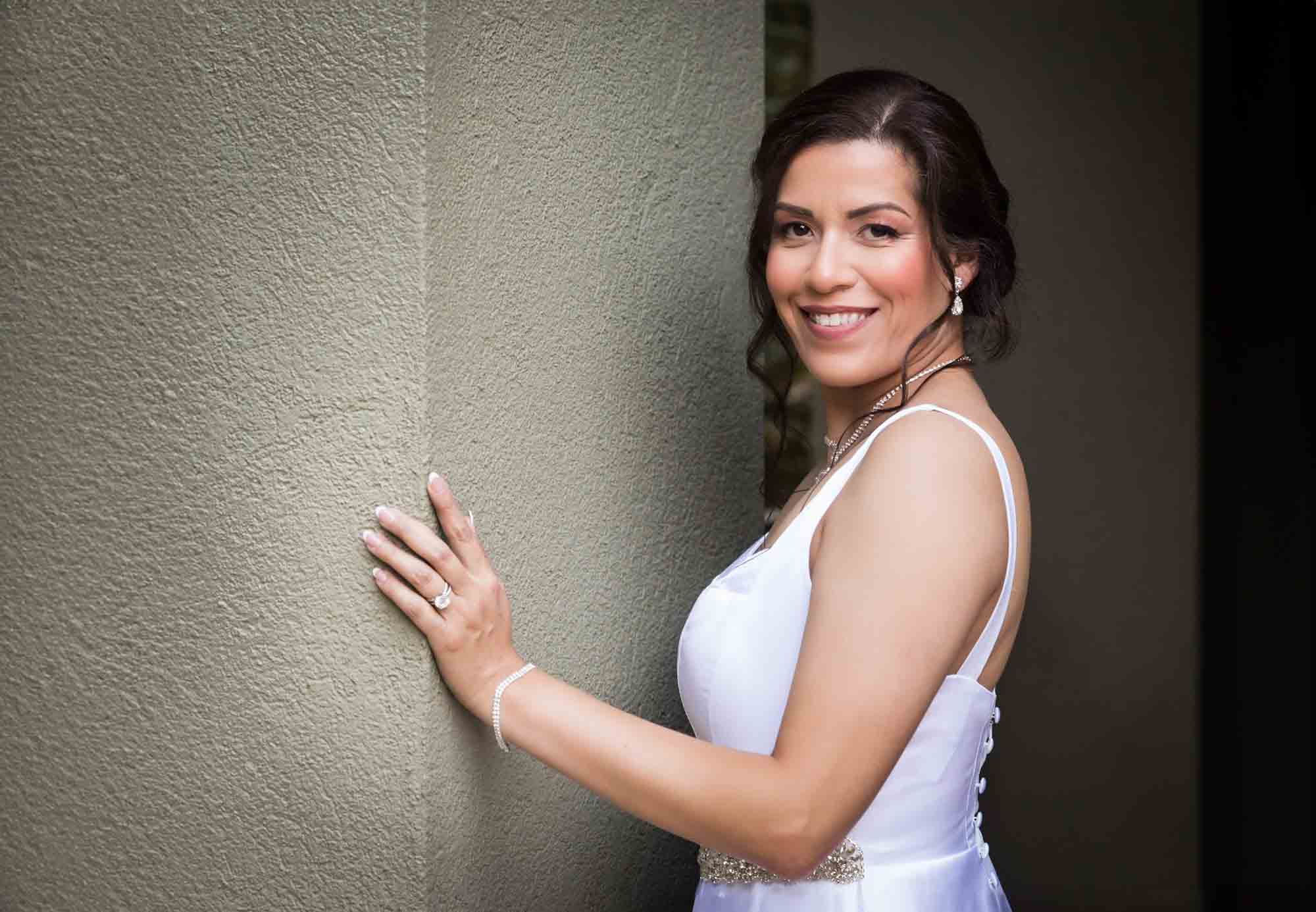 Bride wearing sleeveless, white dress with hand touching green wall during a downtown San Antonio bridal portrait session