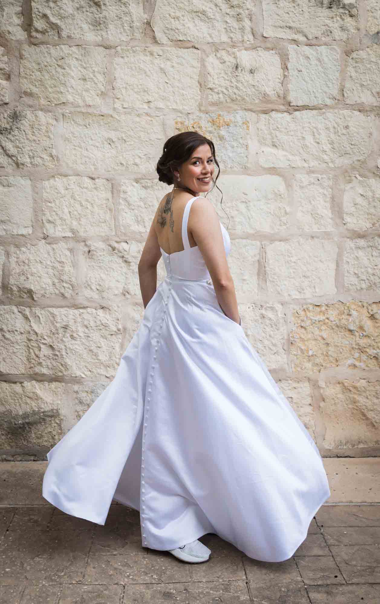 Bride twirling in white, sleeveless dress in front of beige, brick wall for an article about a downtown San Antonio bridal portrait session