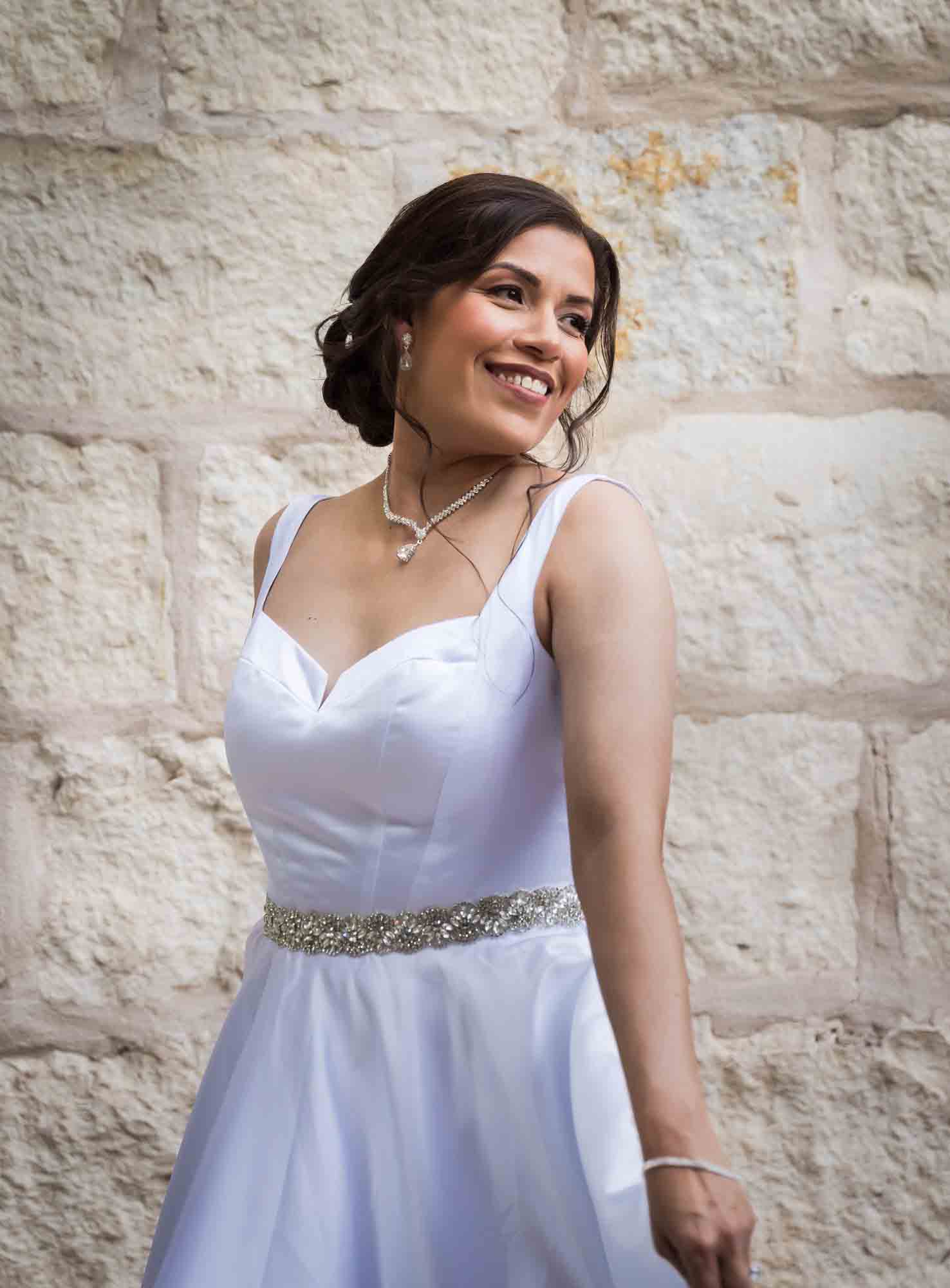 Bride twirling in white, sleeveless dress in front of beige, brick wall for an article about a downtown San Antonio bridal portrait session