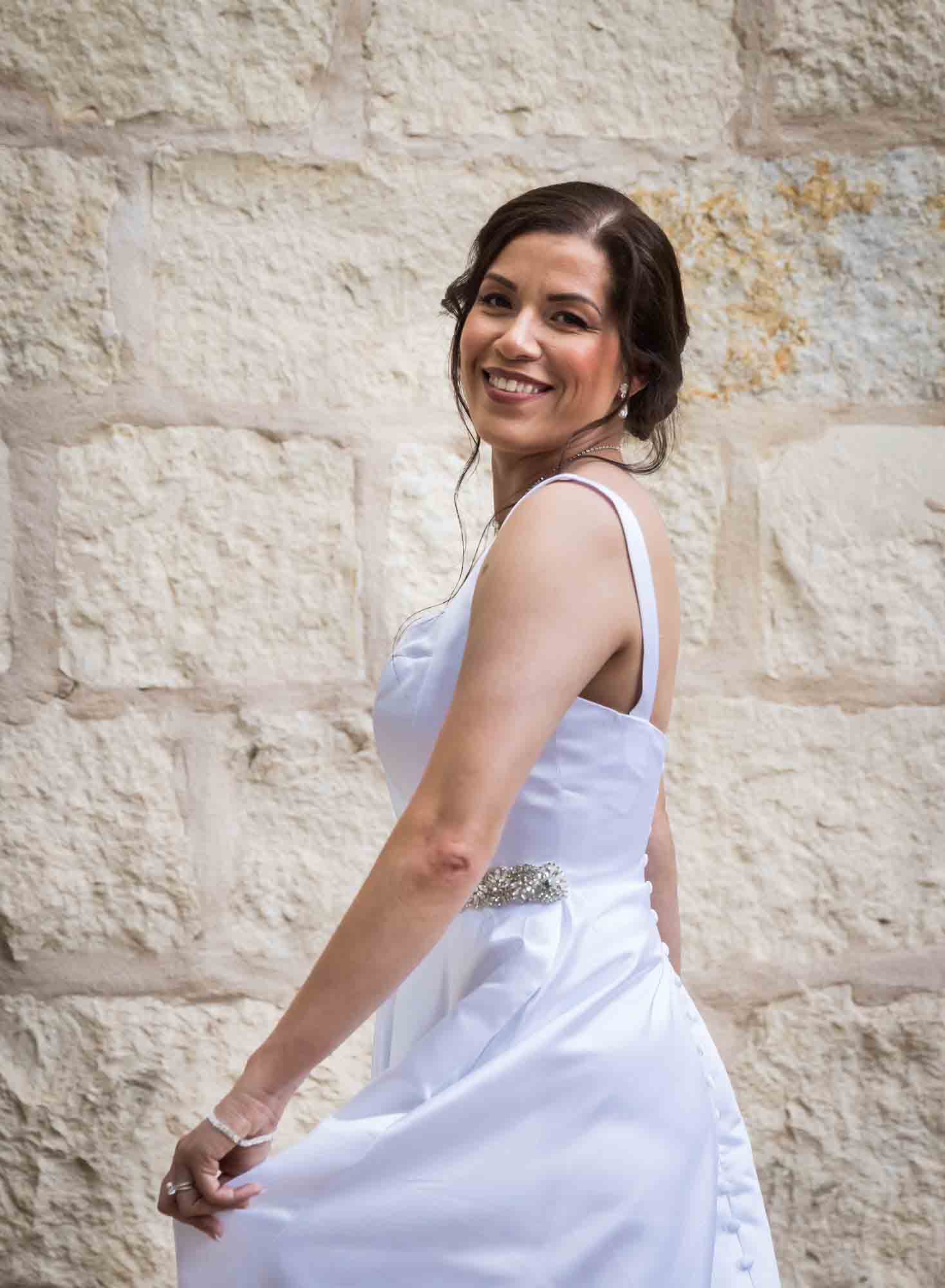 Bride twirling in white, sleeveless dress in front of beige, brick wall for an article about a downtown San Antonio bridal portrait session