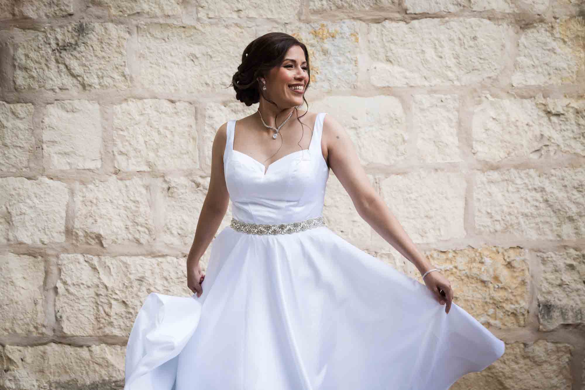 Bride twirling in white, sleeveless dress in front of beige, brick wall for an article about a downtown San Antonio bridal portrait session