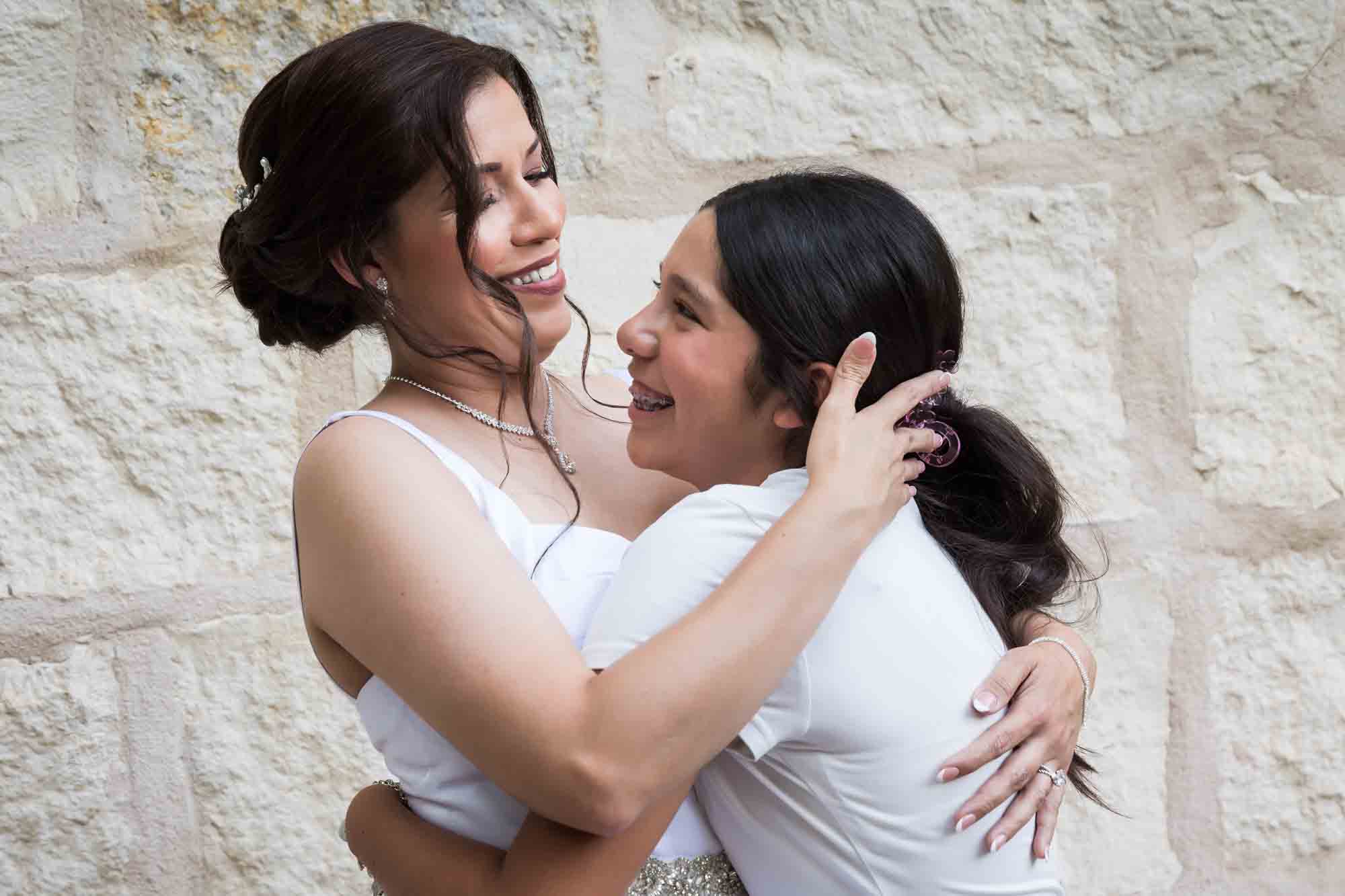 Bride and young girl hugging in front of beige, brick wall during a downtown San Antonio bridal portrait session