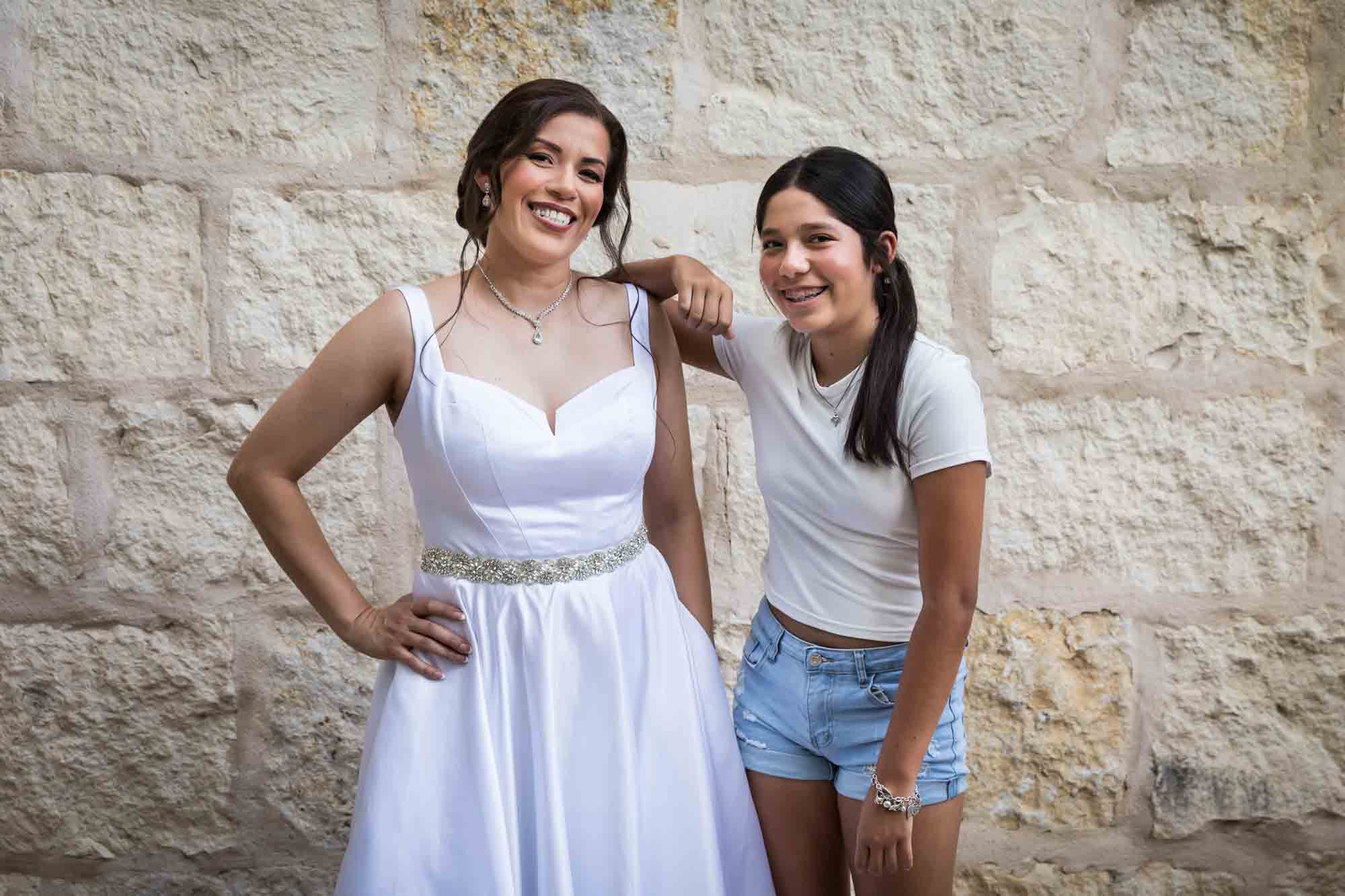 Bride and young girl standing in front of beige, brick wall during a downtown San Antonio bridal portrait session