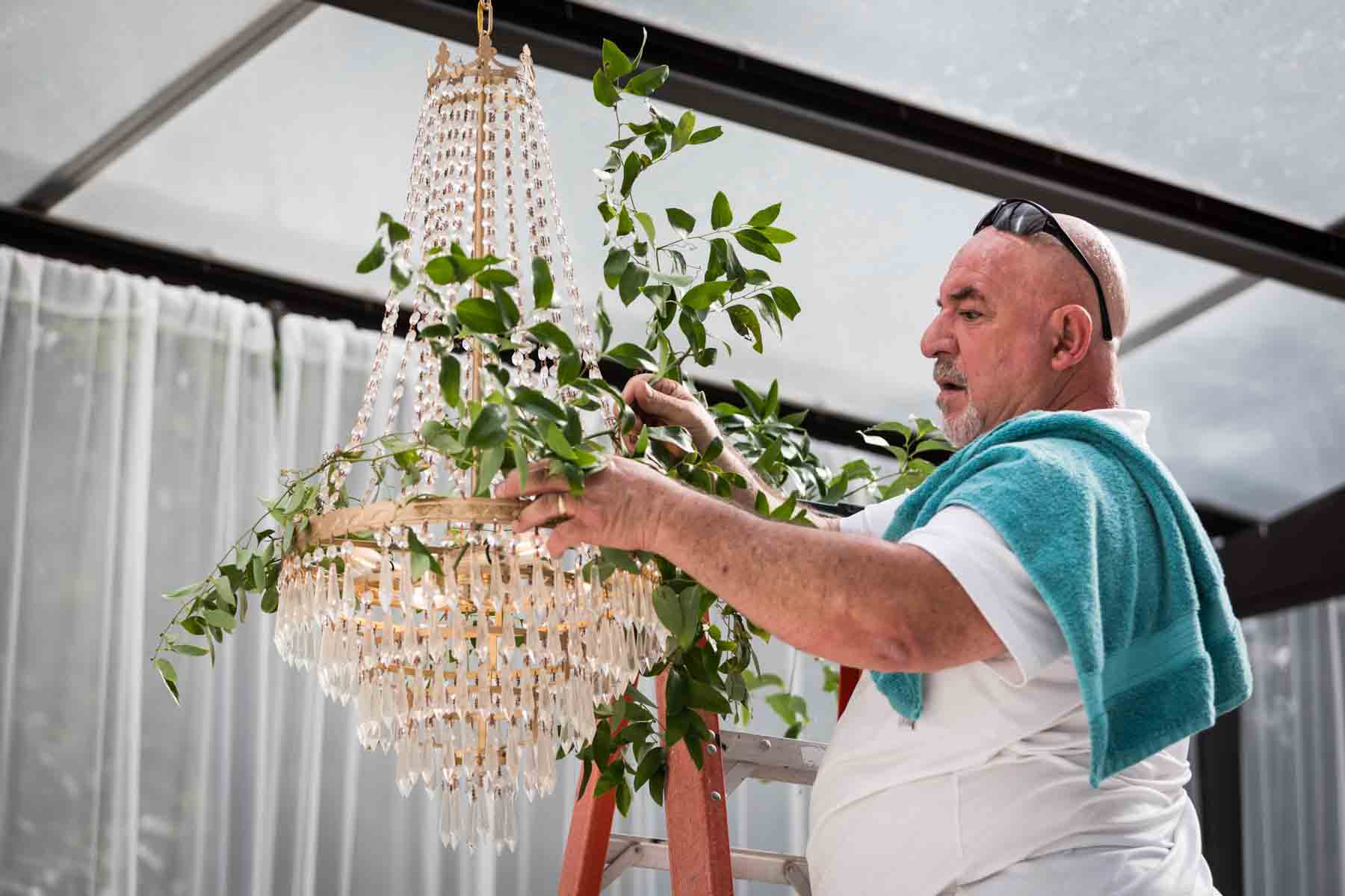 Jose of Ay Poppy! placing greenery in a crystal chandelier for an article on how to choose the perfect flowers for your wedding or event