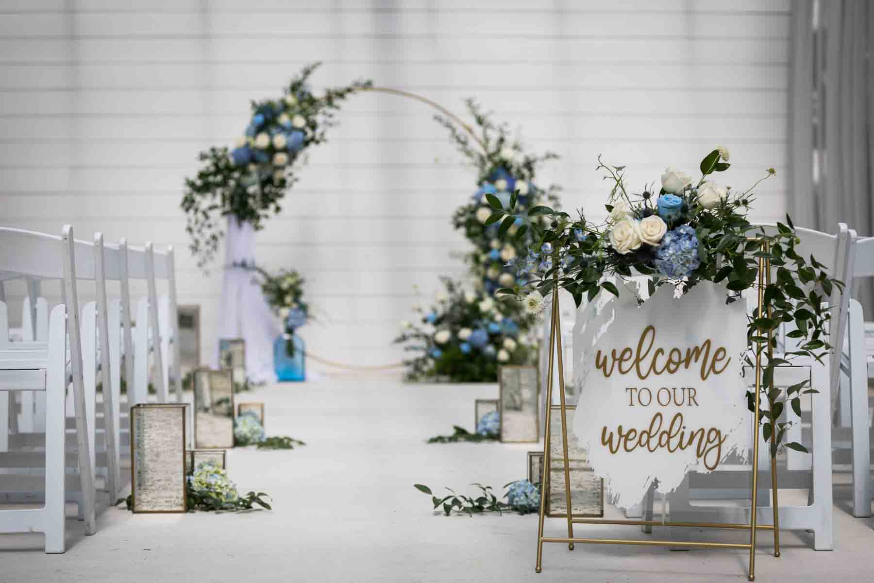 Finished white and blue wedding ceremony floral display with 'Welcome to Our Wedding' sign for an article on how to choose the perfect flowers for your wedding or event