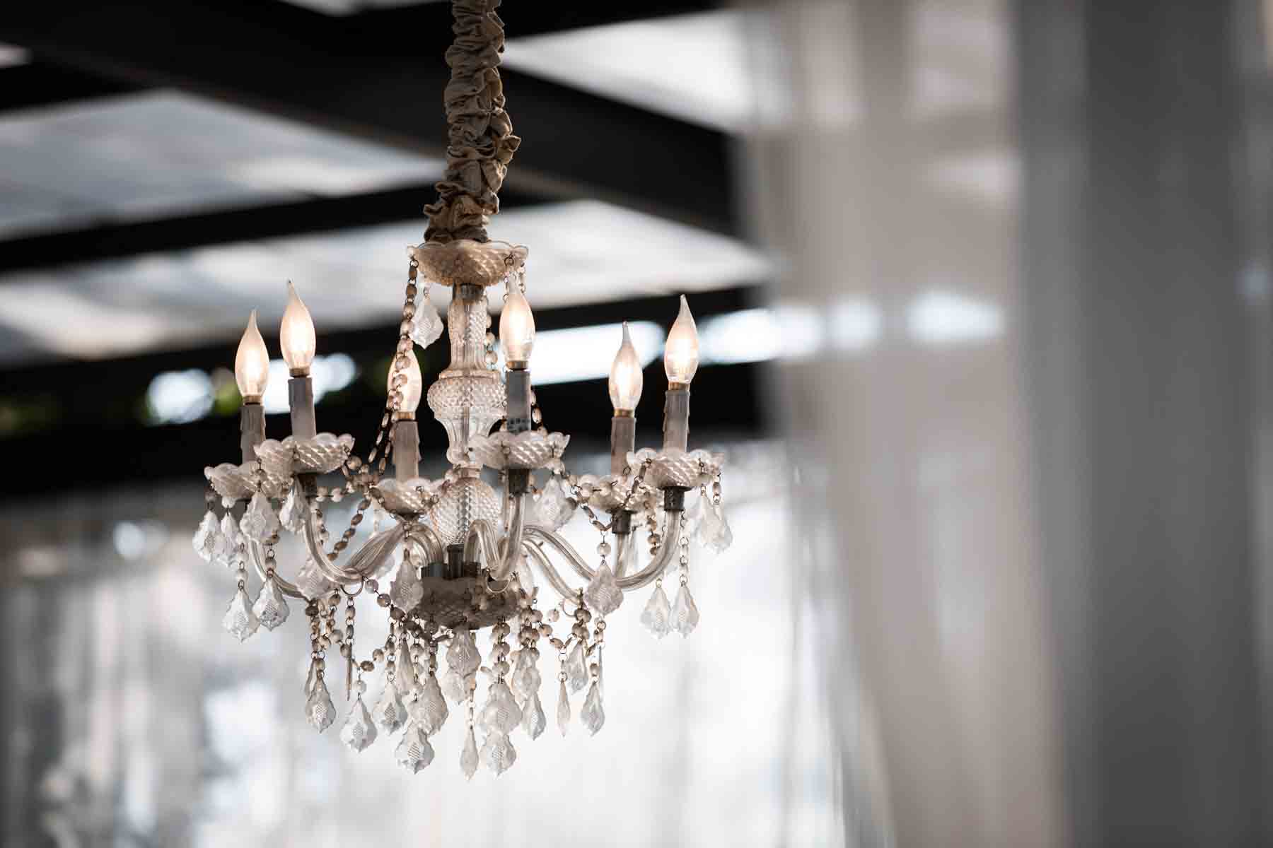 Chandelier with many lights and hanging crystals hanging from ceiling with white curtain on the side