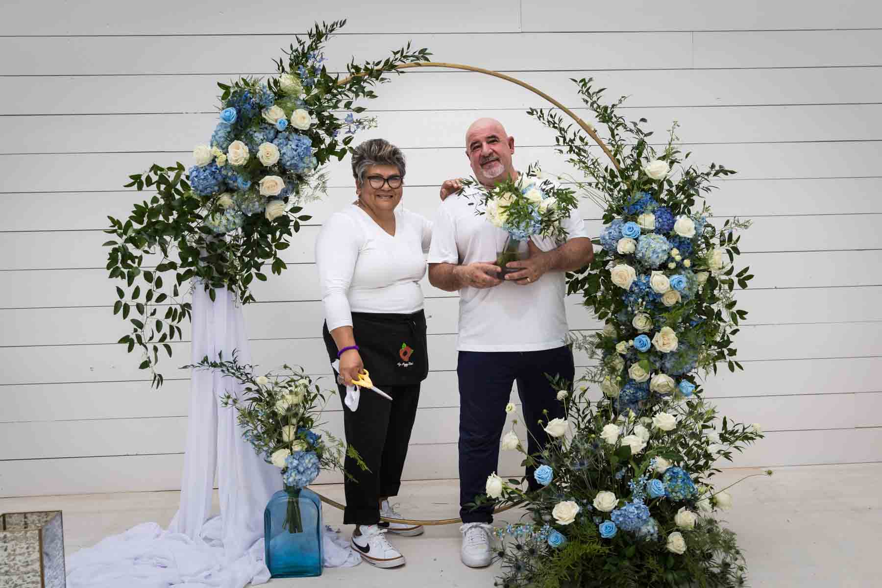 Cici and Jose of Ay Poppy! Floral and Event Decor in front of a white and blue wedding ceremony display