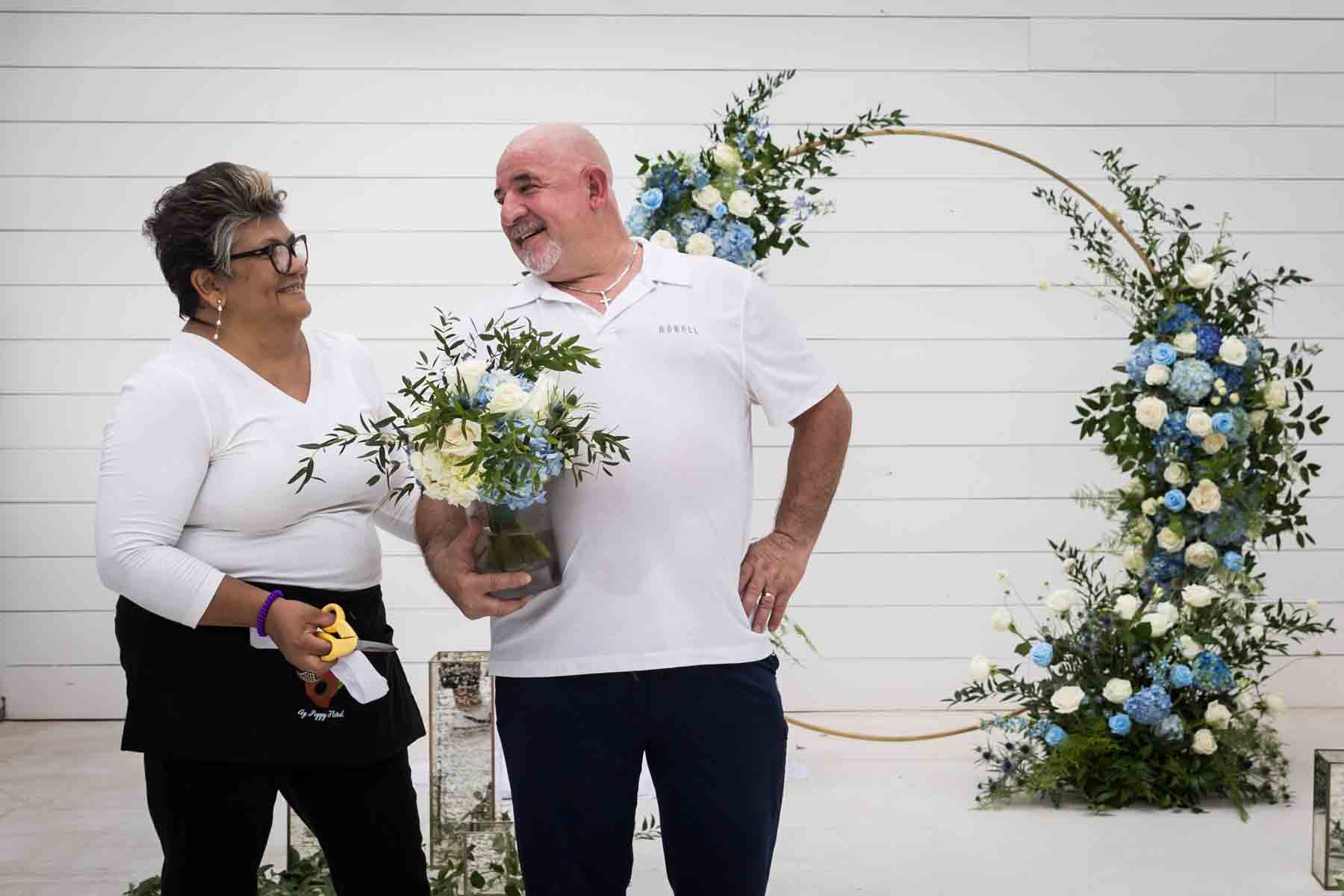 Cici and Jose of Ay Poppy! Floral and Event Decor in front of a white and blue wedding ceremony display