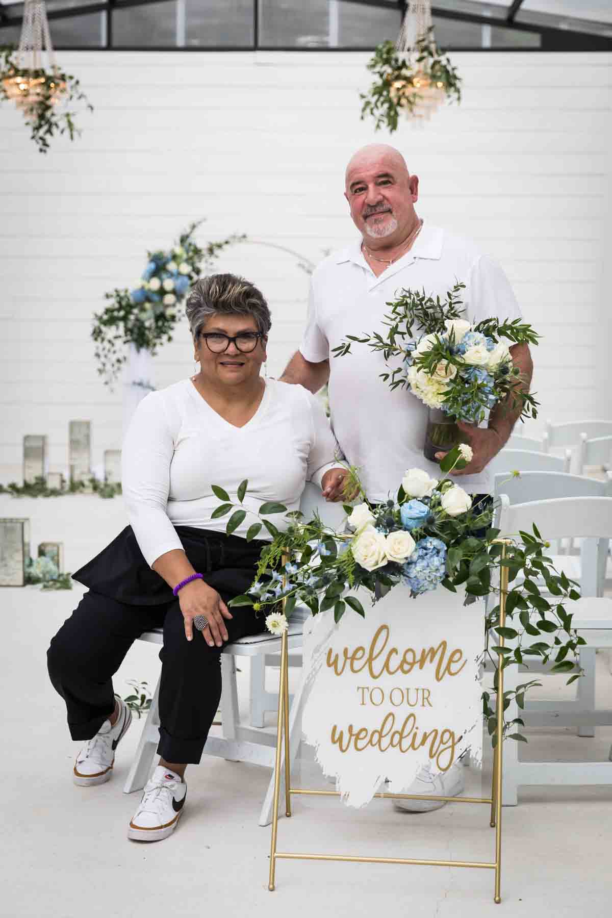 Cici and Jose of Ay Poppy! Floral and Event Decor in front of a white and blue wedding ceremony display