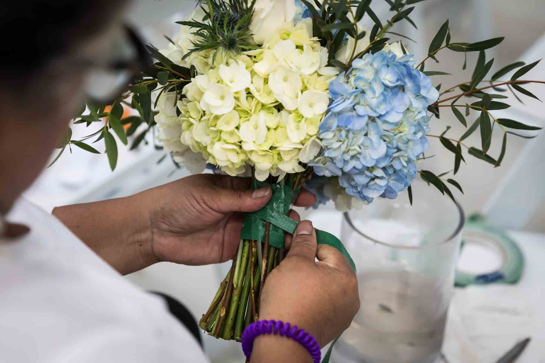 Close up of woman using floral tape to create a white and blue bridal bouquet for an article on how to choose the perfect flowers for your wedding or event