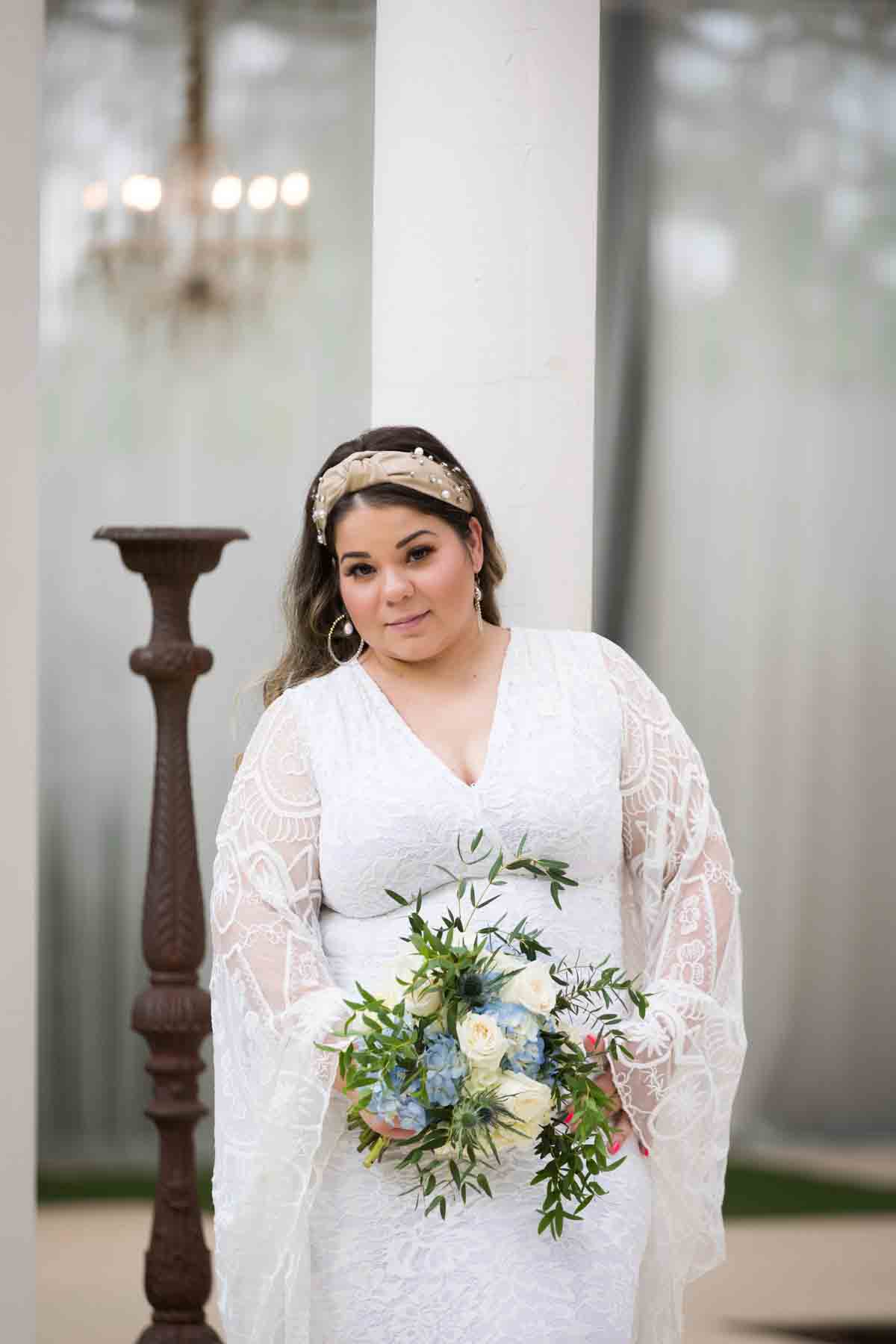 Bride with long sleeves holding a white and blue bridal bouquet in front of bronze candelabra and chandelier