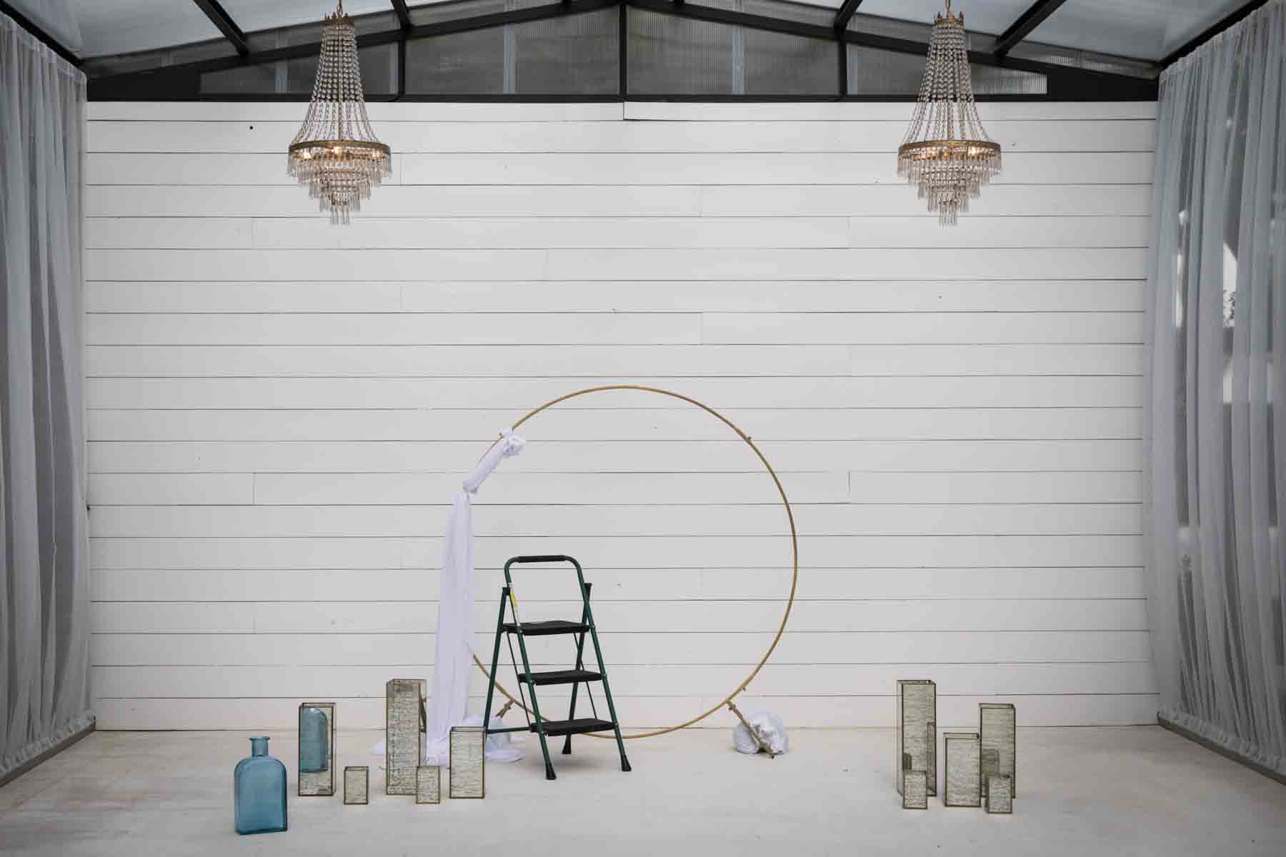 Empty room with two chandeliers hanging overhead, small stool, and brass floral form before florist begins for an article on how to choose the perfect flowers for your wedding or event