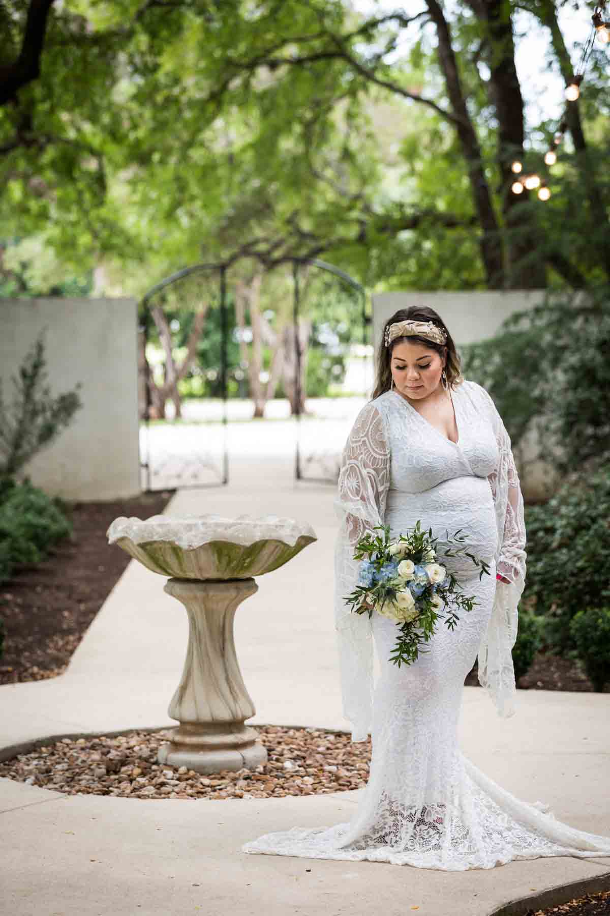 Bride looking down at bouquet to the right of stone bird bath for an article on how to choose the perfect flowers for your wedding or event