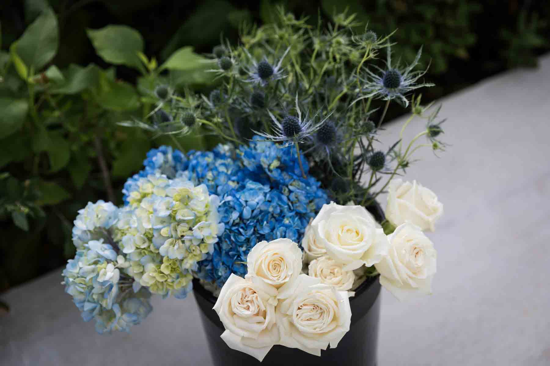 Close up of white and blue flowers sitting in a black bucket on the ground for an article on how to choose the perfect flowers for your wedding or event