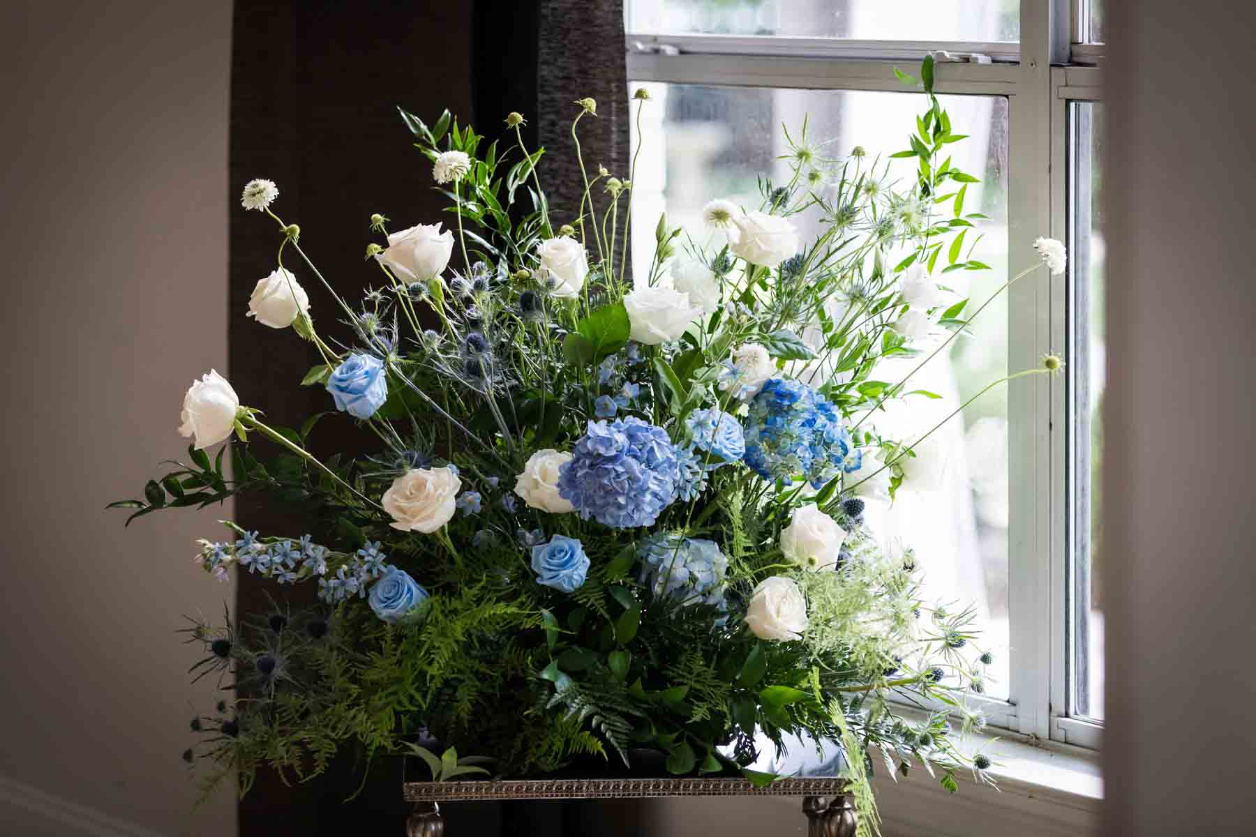 Close up of white and blue flower centerpiece in front of a window with grey curtains for an article on how to choose the perfect flowers for your wedding or event