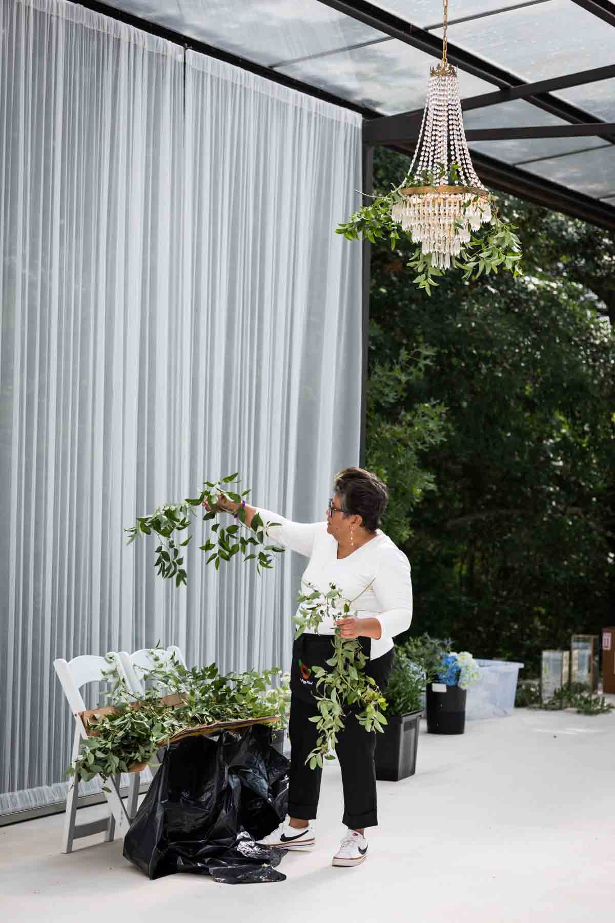 Cici of Ay Poppy! inspecting a piece of greenery below a crystal chandelier for an article on how to choose the perfect flowers for your wedding or event