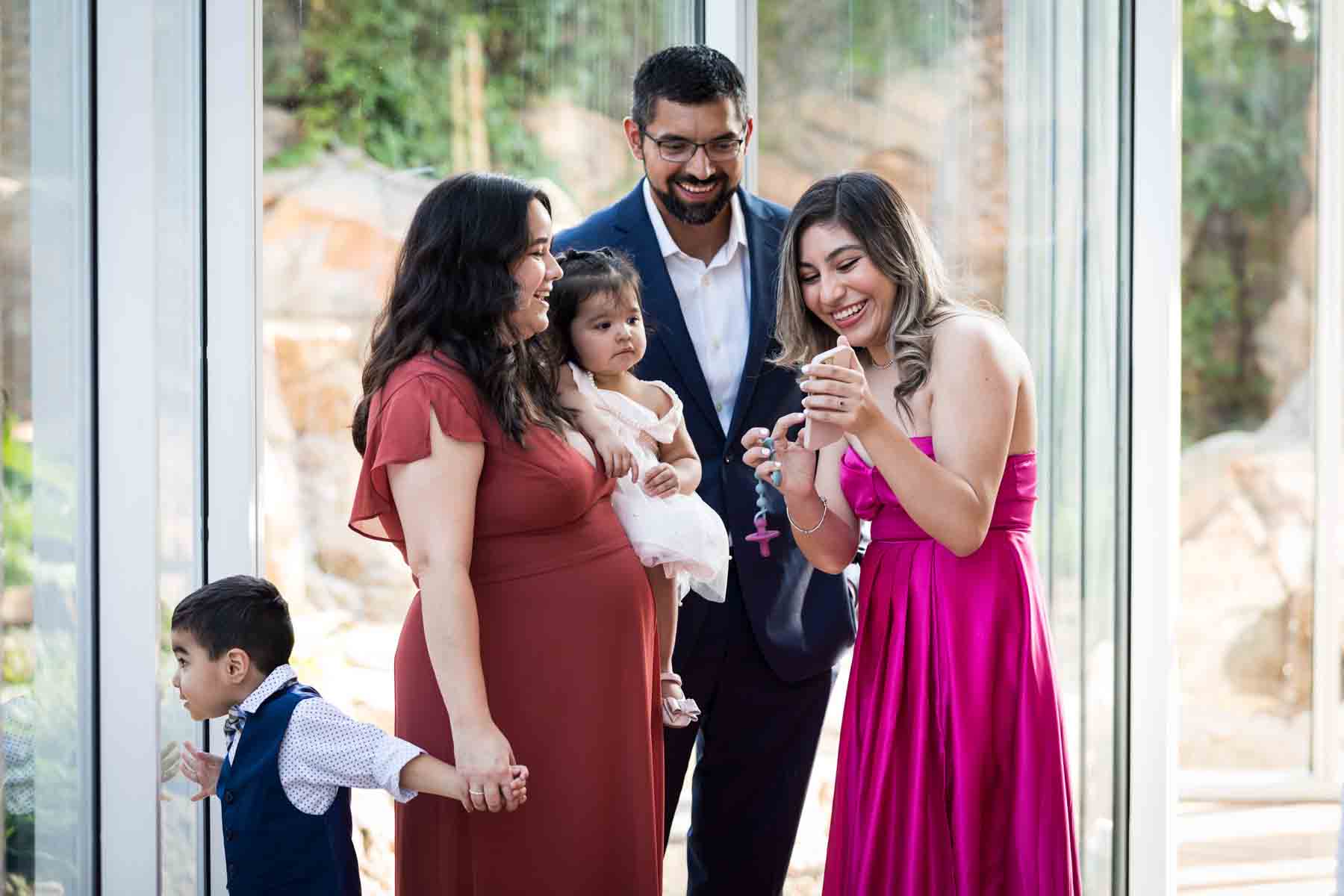 Woman in pink dress showing cell phone to family with two children in front of a window