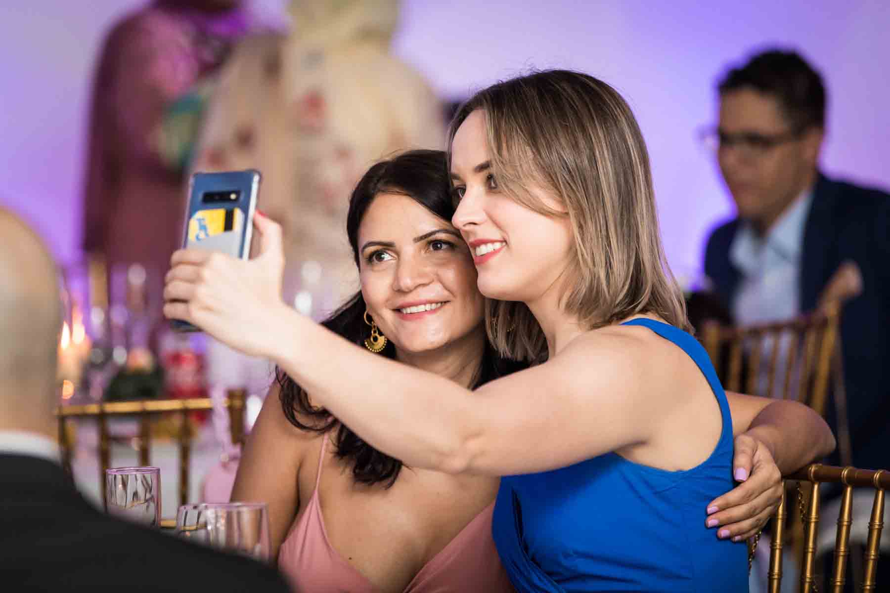 Two women taking a selfie at a wedding reception for an article on how to take the perfect selfie