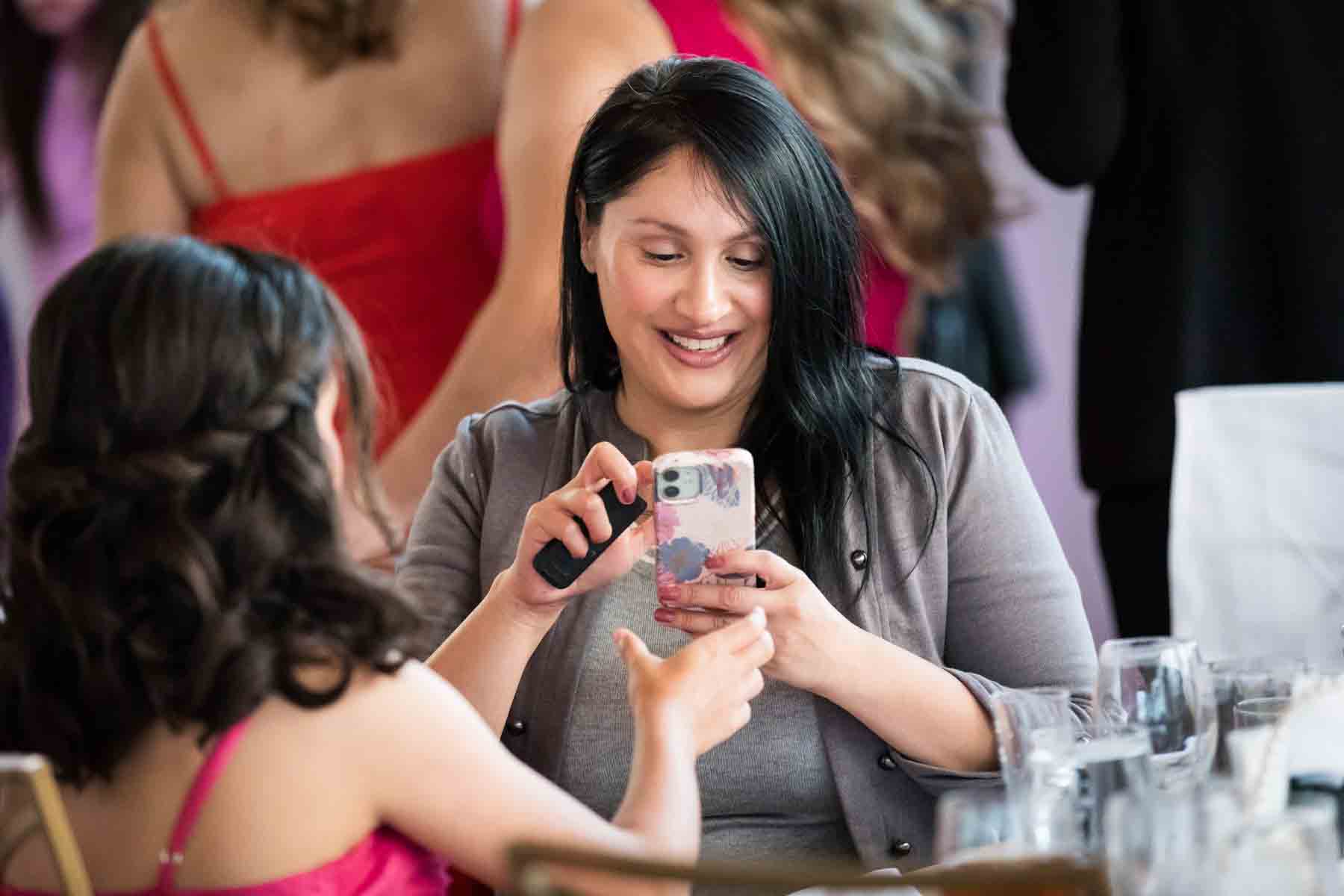 Woman with dark brown hair seated at a table looking at her cell phone