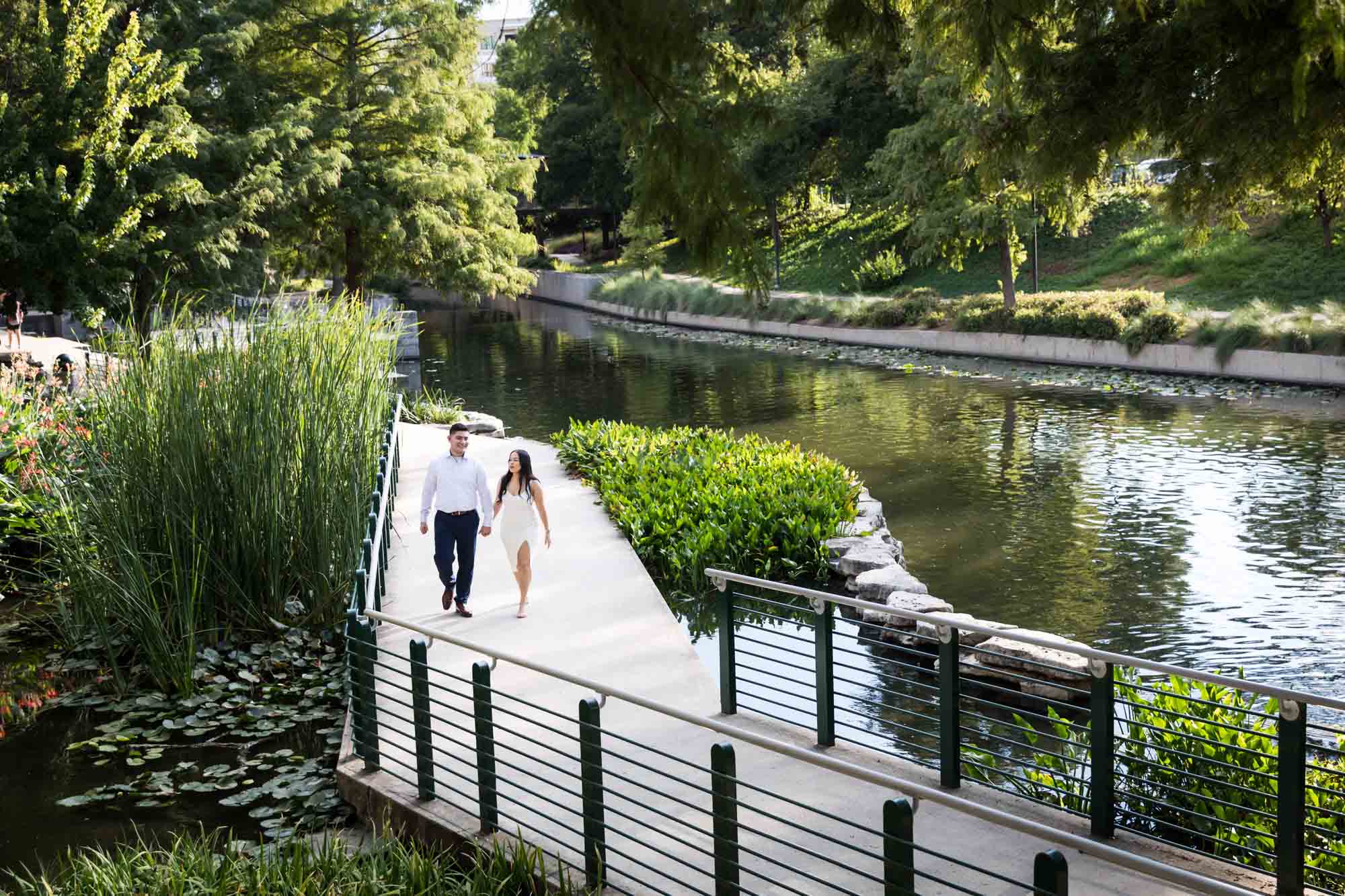 Couple holding hands and walking on pathway beside River Walk for an article on Pearl surprise proposal tips