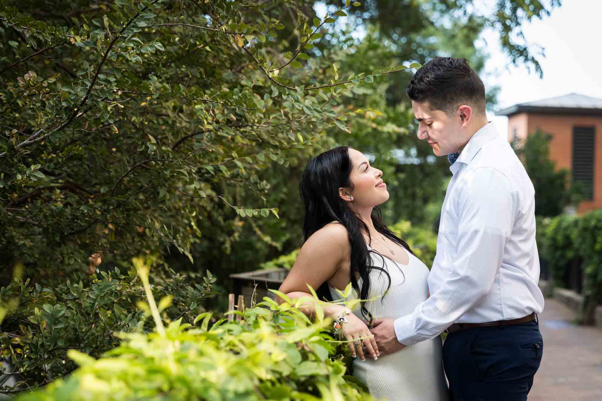 Couple leaning against railing covered in green vines during a Pearl engagement photo shoot