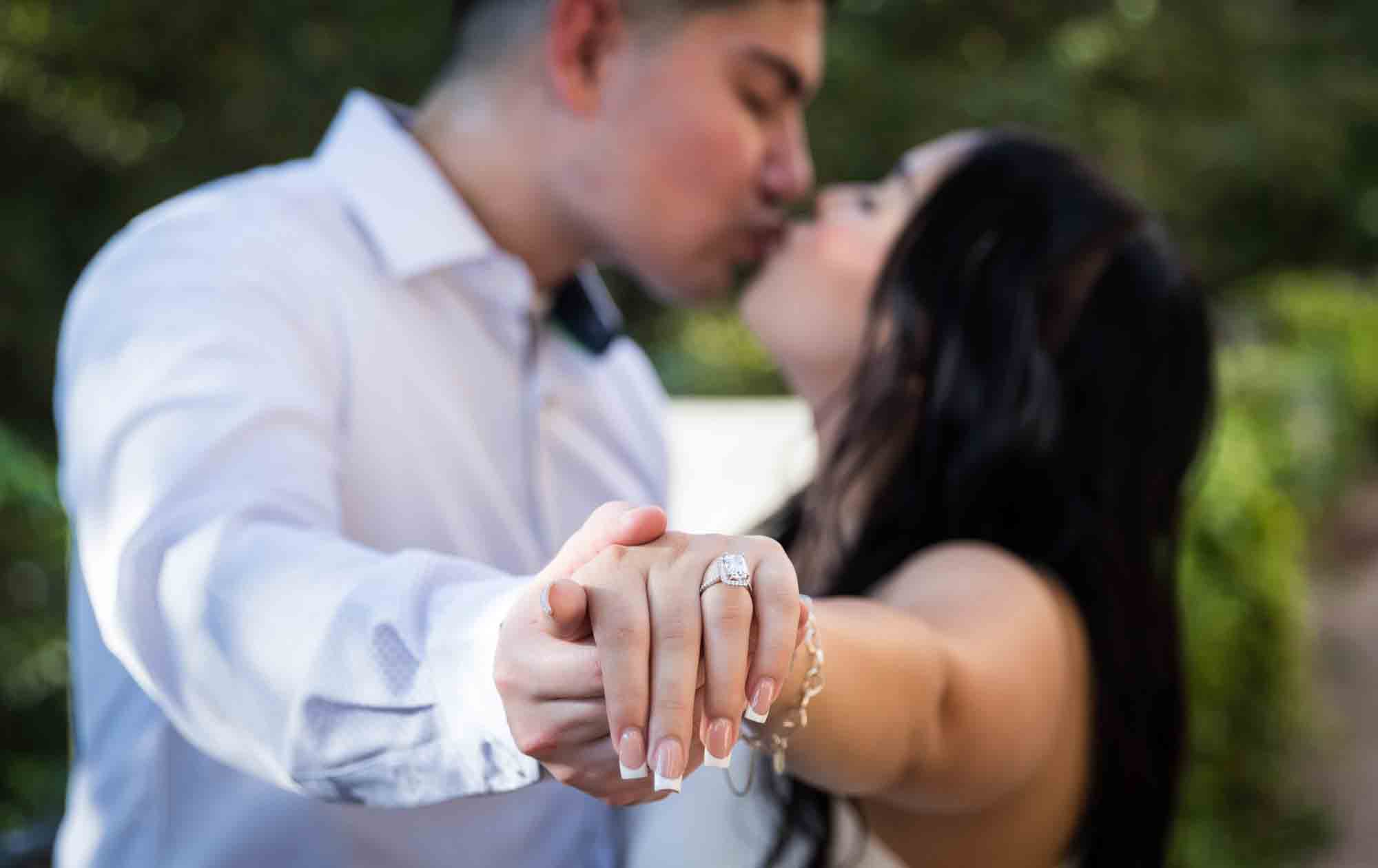 Couple kissing and holding out hands showing woman wearing engagement ring during a Pearl engagement photo shoot