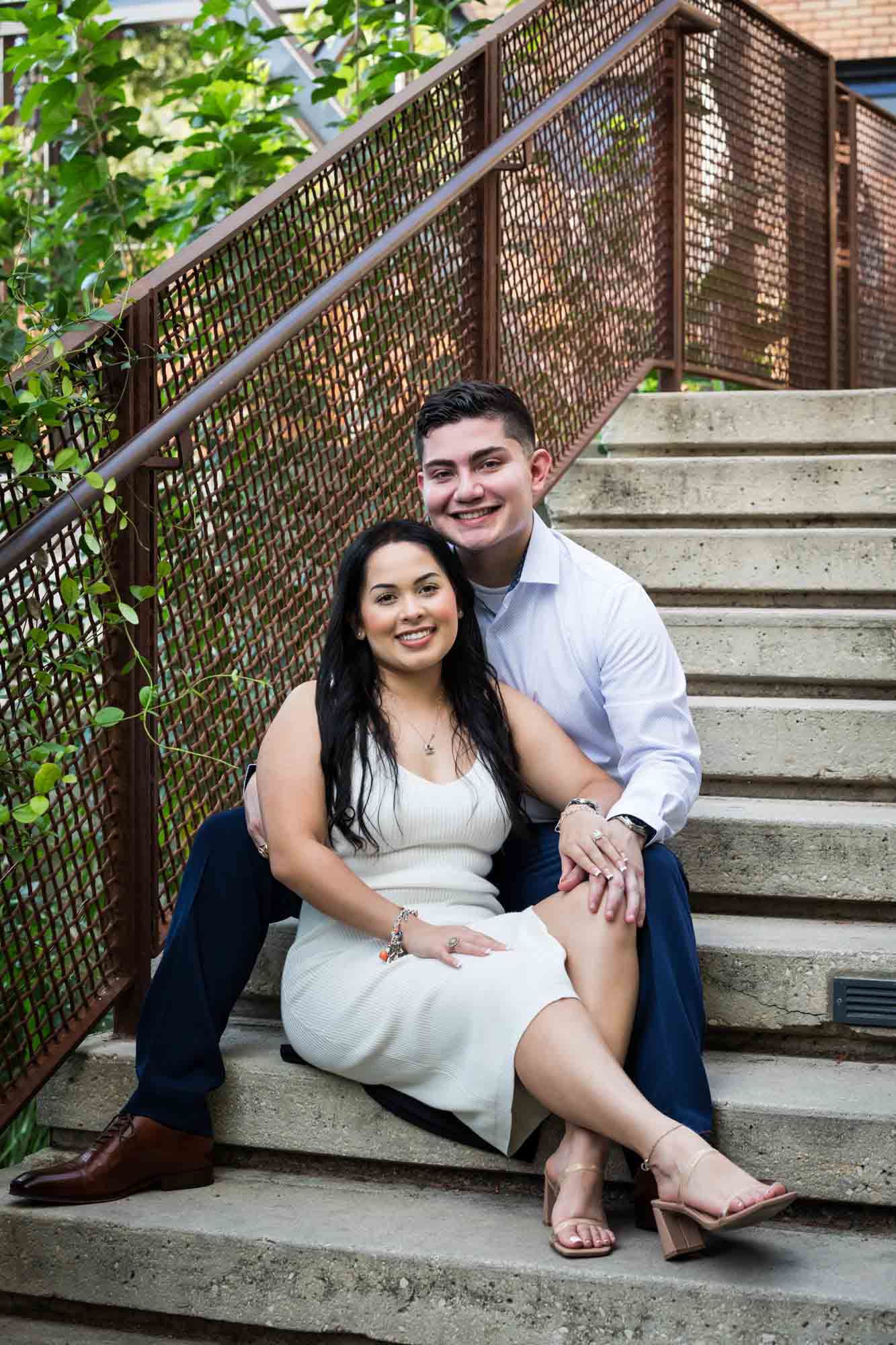 Couple sitting on stone stairs in front of metal railing during a Pearl engagement photo shoot