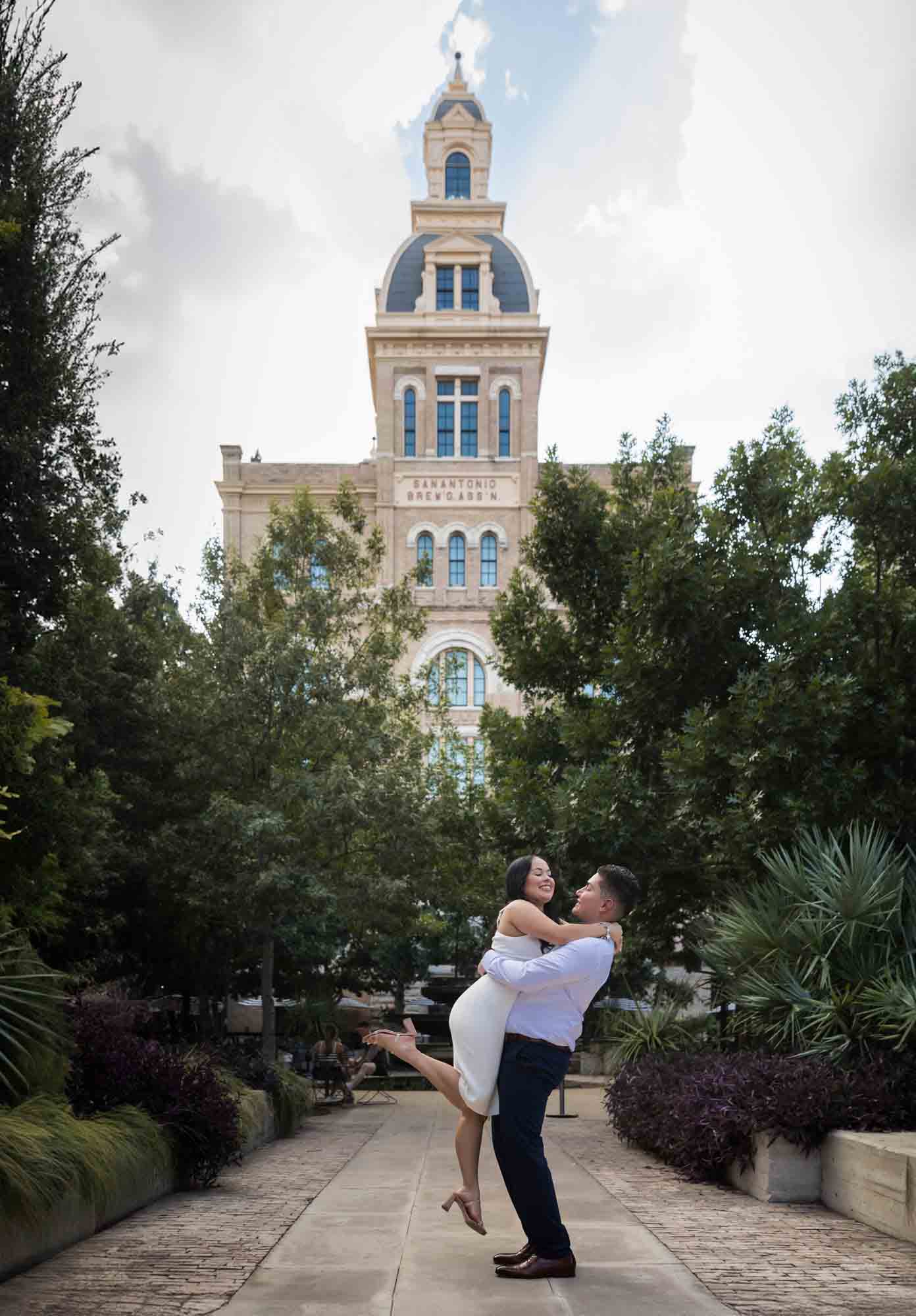 Man lifting woman in the air in front of Pearl Brewery building during a Pearl engagement photo shoot