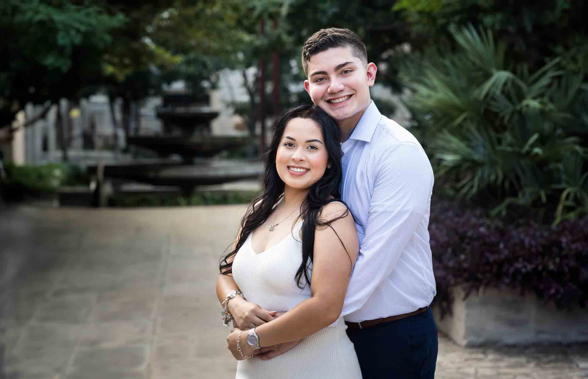 Couple huggingon sidewalk in front of palm tree during a Pearl engagement photo shoot